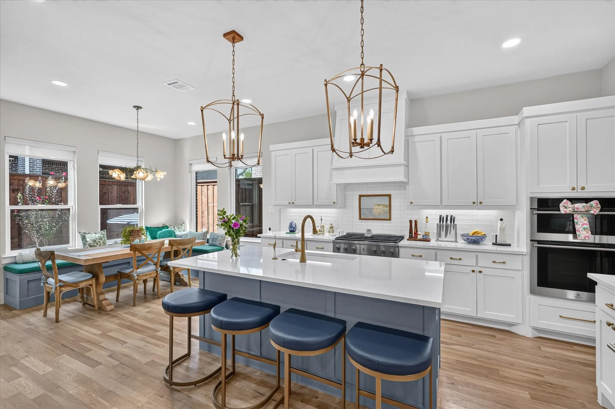 Kitchen featuring white shaker cabinetry, gold-finish hardware, a large kitchen island with a white countertop, wood-finish flooring, and a built-in wall oven