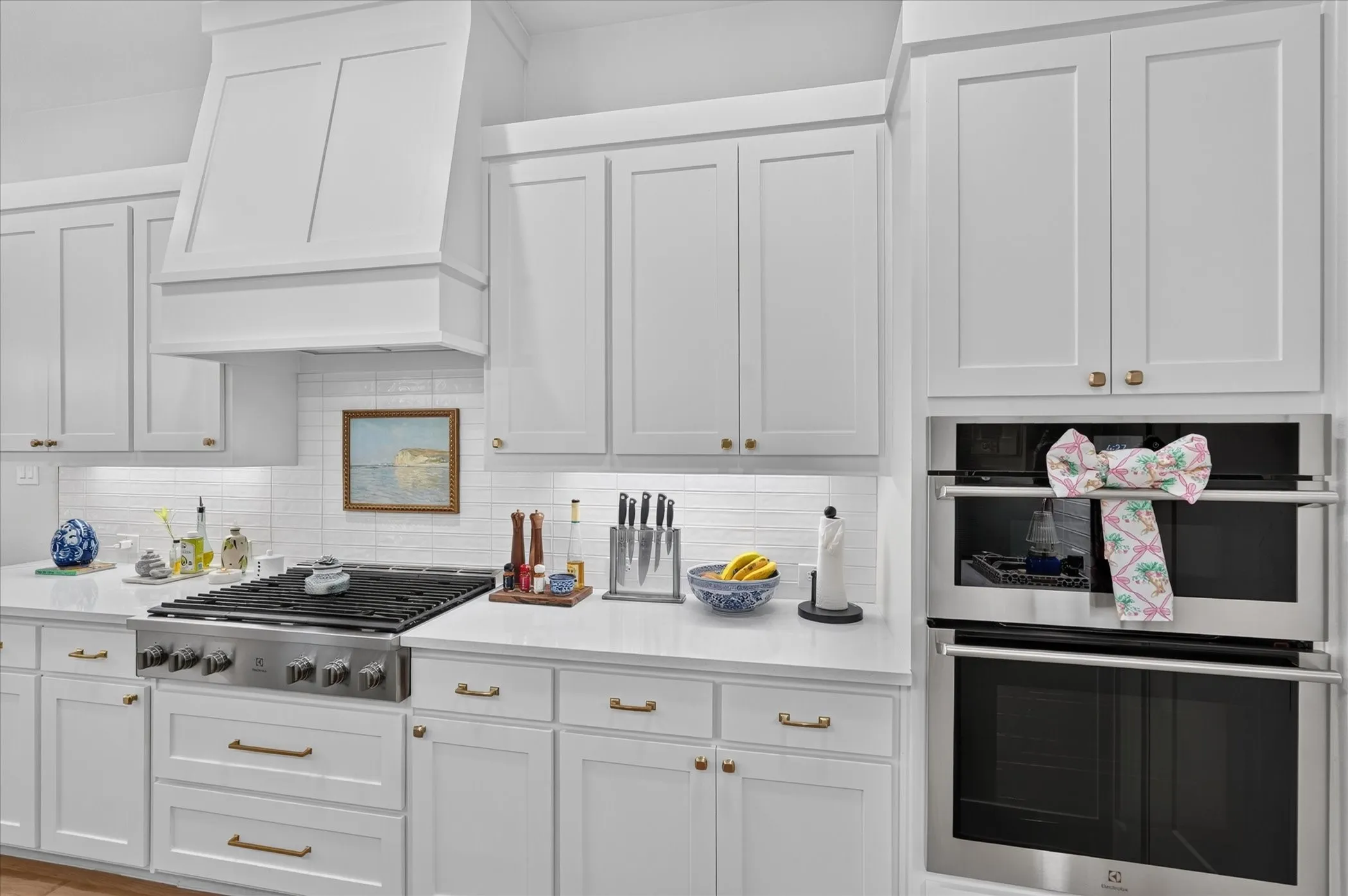 White shaker-style cabinetry with gold-tone hardware, professional-grade stainless steel range, white subway tile backsplash, built-in double oven, and under-cabinet lighting