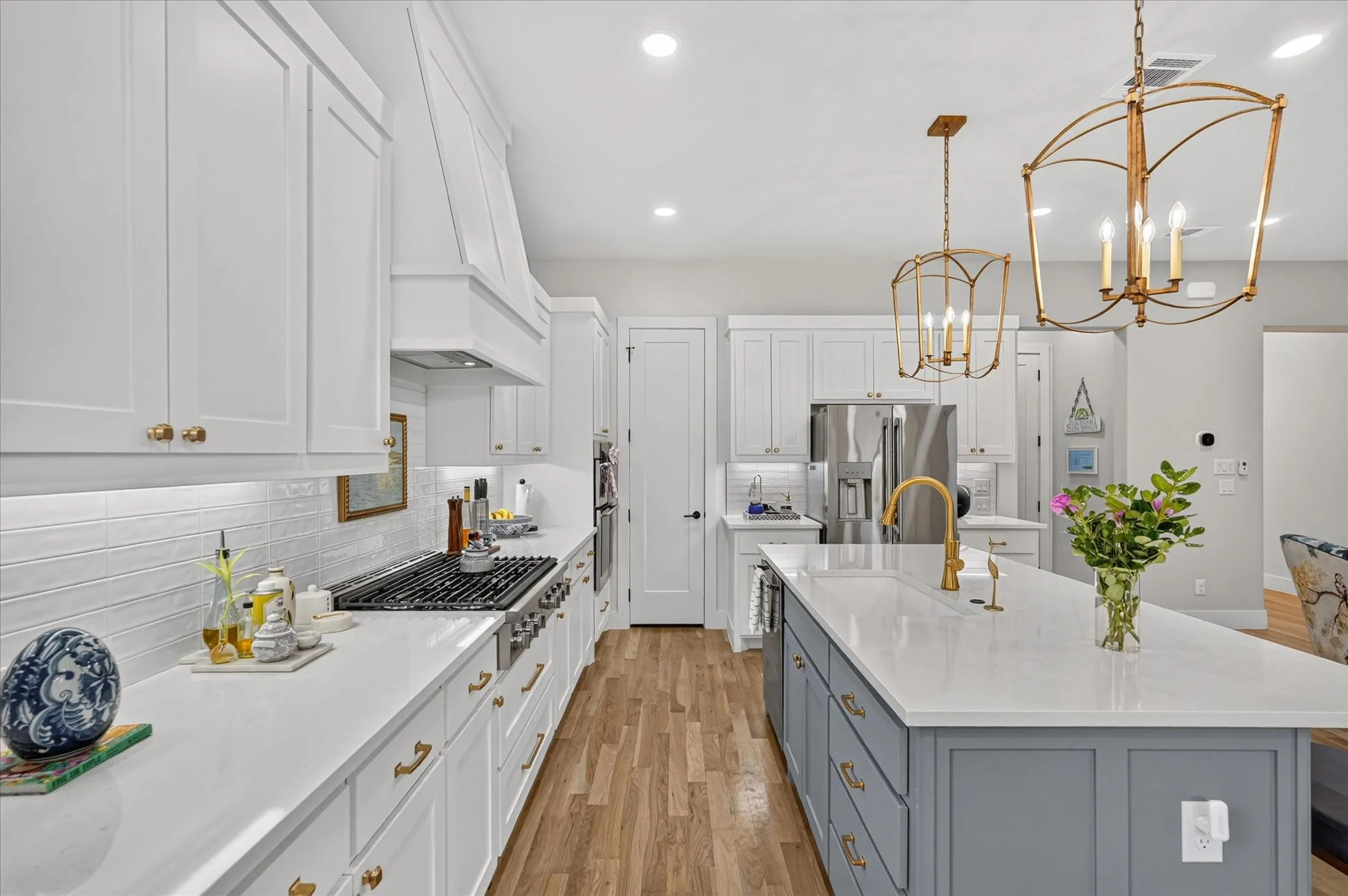 Kitchen featuring white shaker cabinetry, an expansive center island with a stone countertop, wood-finish flooring, a professional-grade range, and brushed gold fixtures