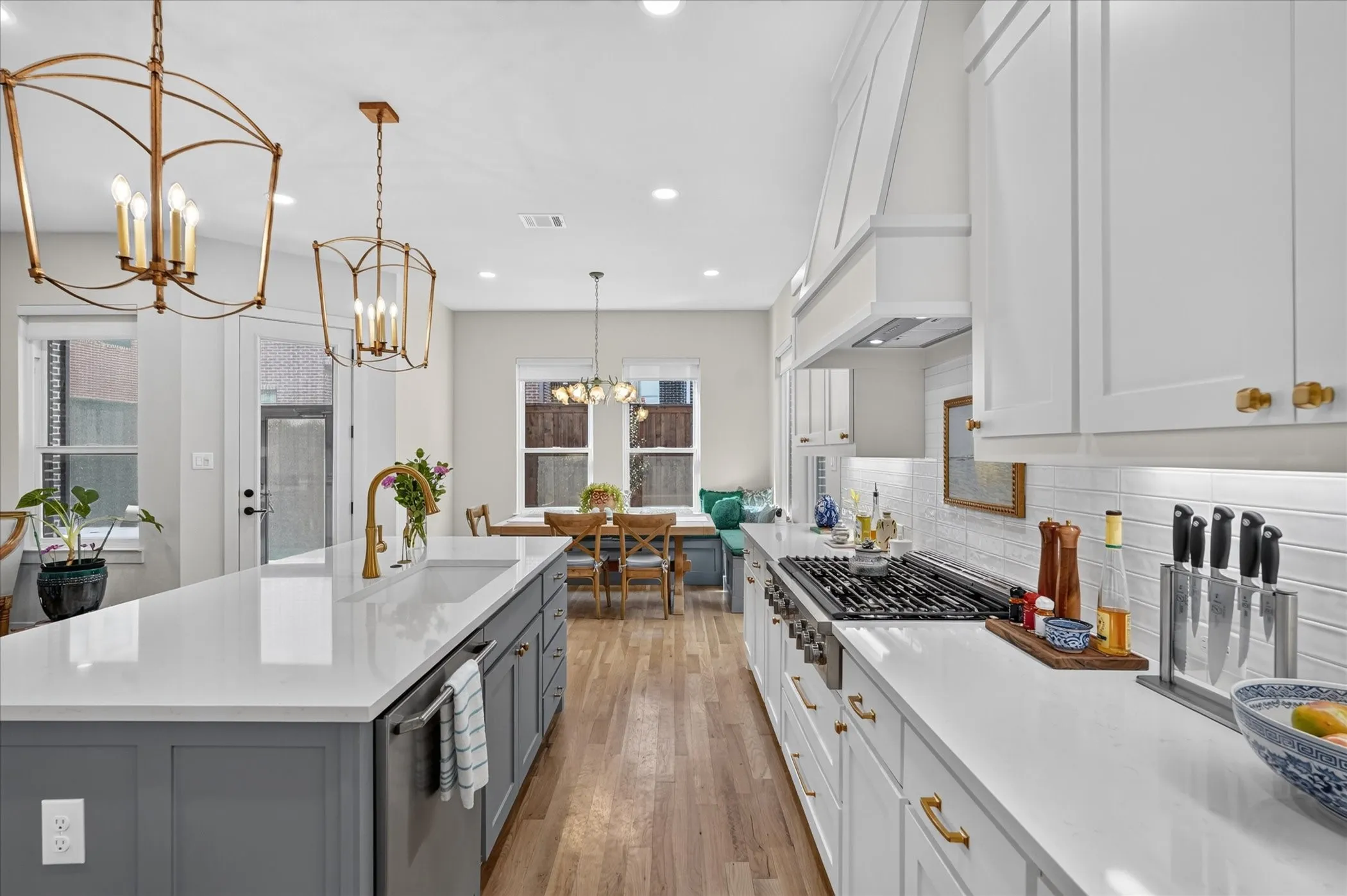 Spacious kitchen featuring an extended island with a built-in sink, white cabinetry with gold-finish hardware, stainless steel range, and wood-finish flooring