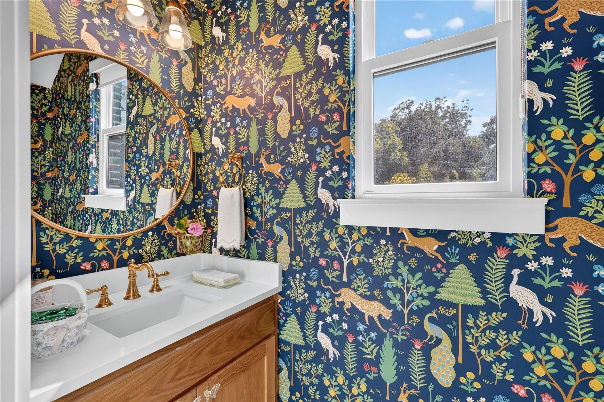 Single-pane window, vanity with integrated sink, gold-finish faucet, circular mirror, and wall-mounted light fixture