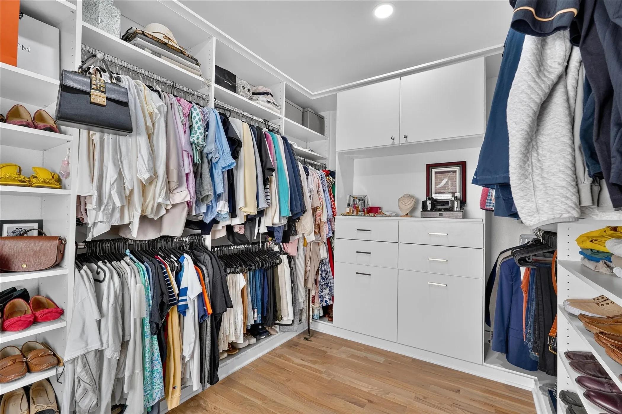 Built-in custom closet system with white cabinetry, integrated shelving, hanging rods, and wood-finish flooring