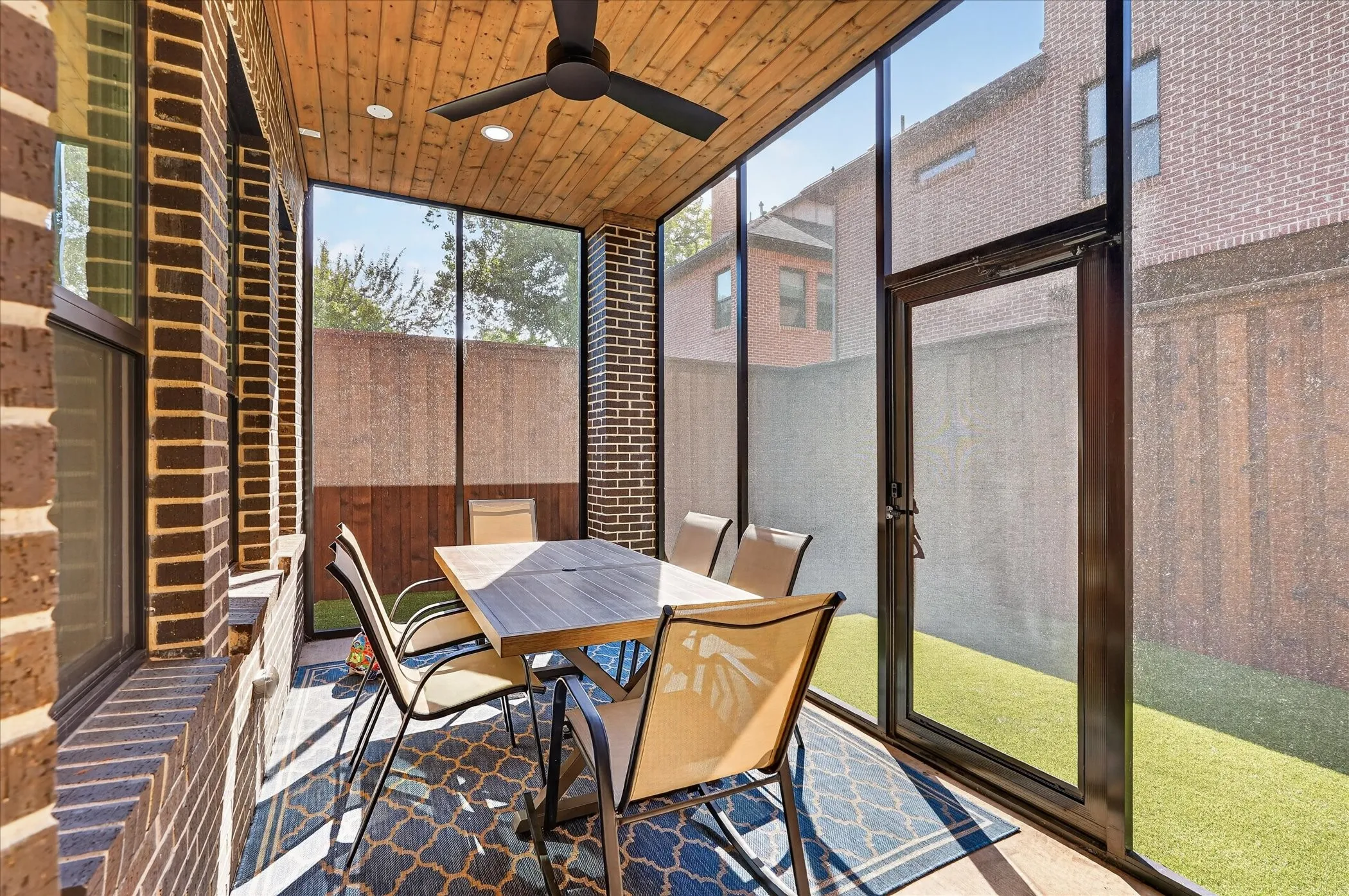 Screened patio featuring a wood-paneled ceiling, ceiling fan, and brick wall accents