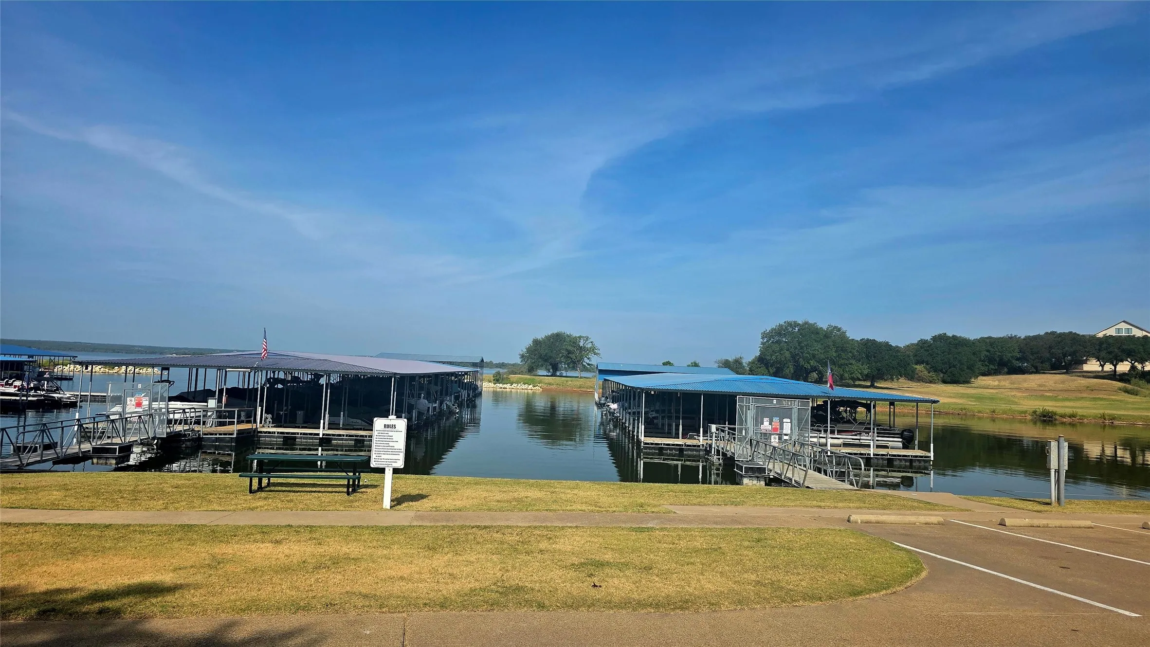 Covered boat slips with blue roofs, a paved boat ramp, and a grassy shoreline