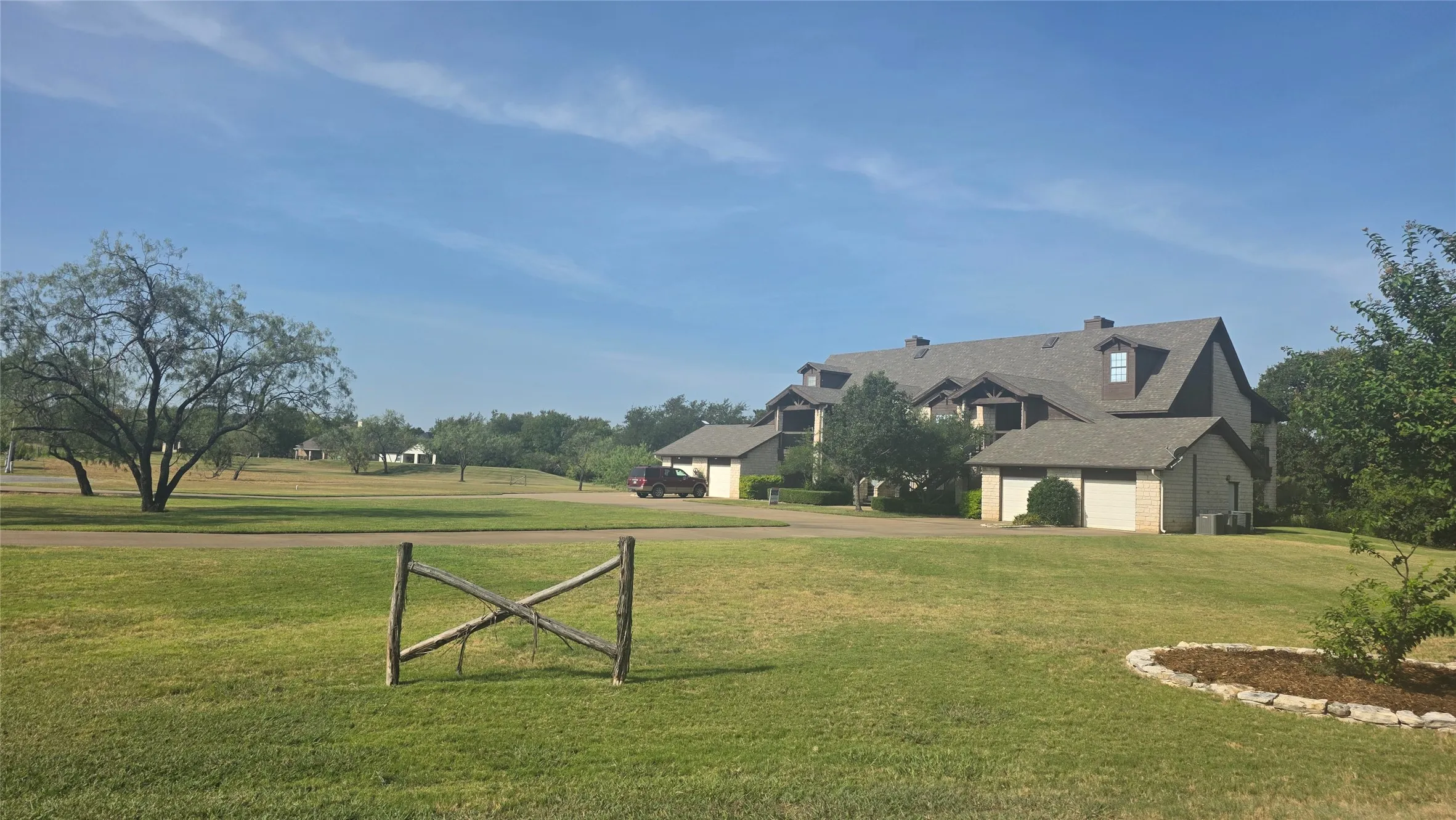Expansive green lawn with mature trees and a gravel driveway