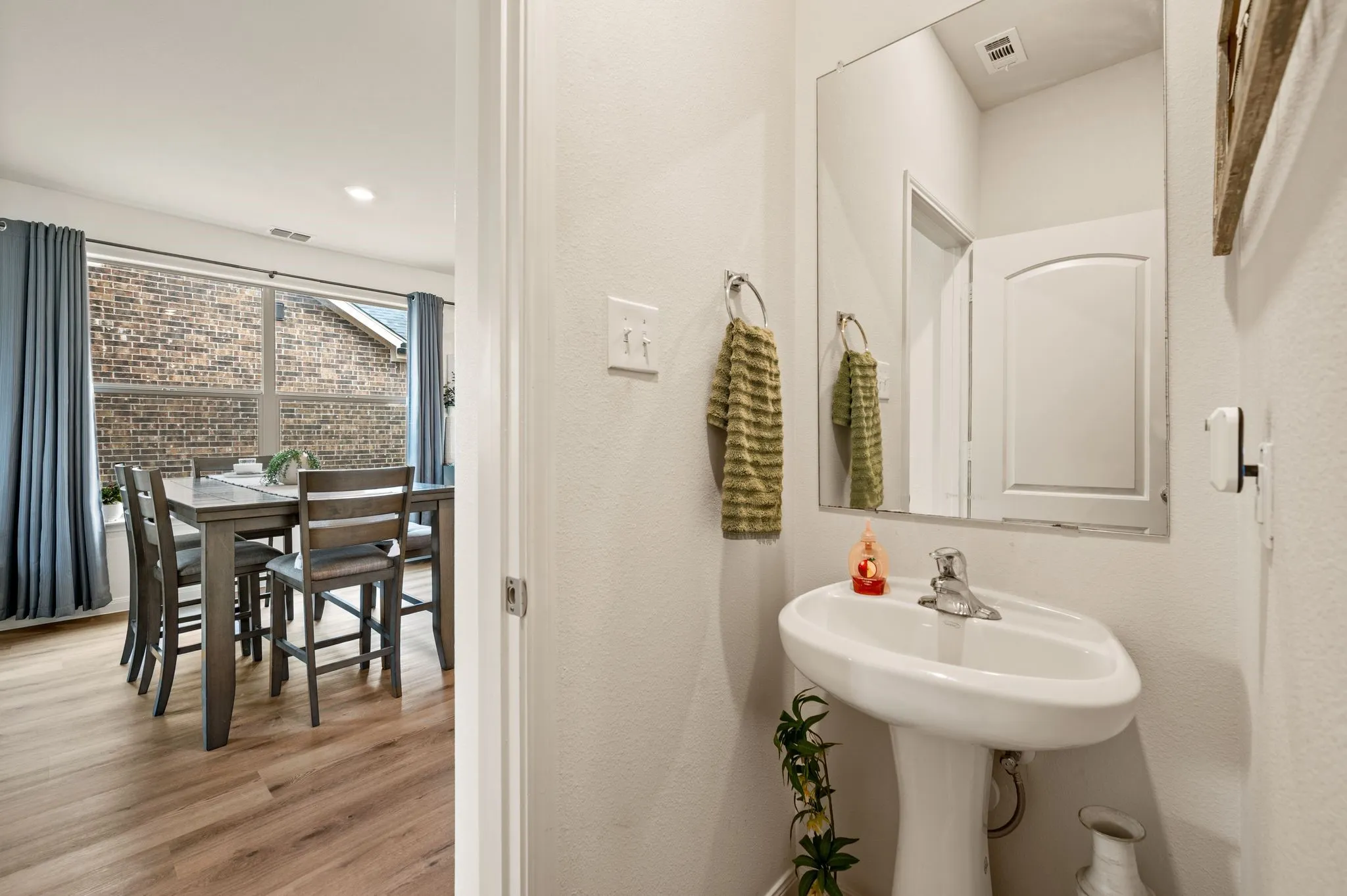 Pedestal sink with single-handle faucet, wall-mounted mirror, and wood-finish flooring