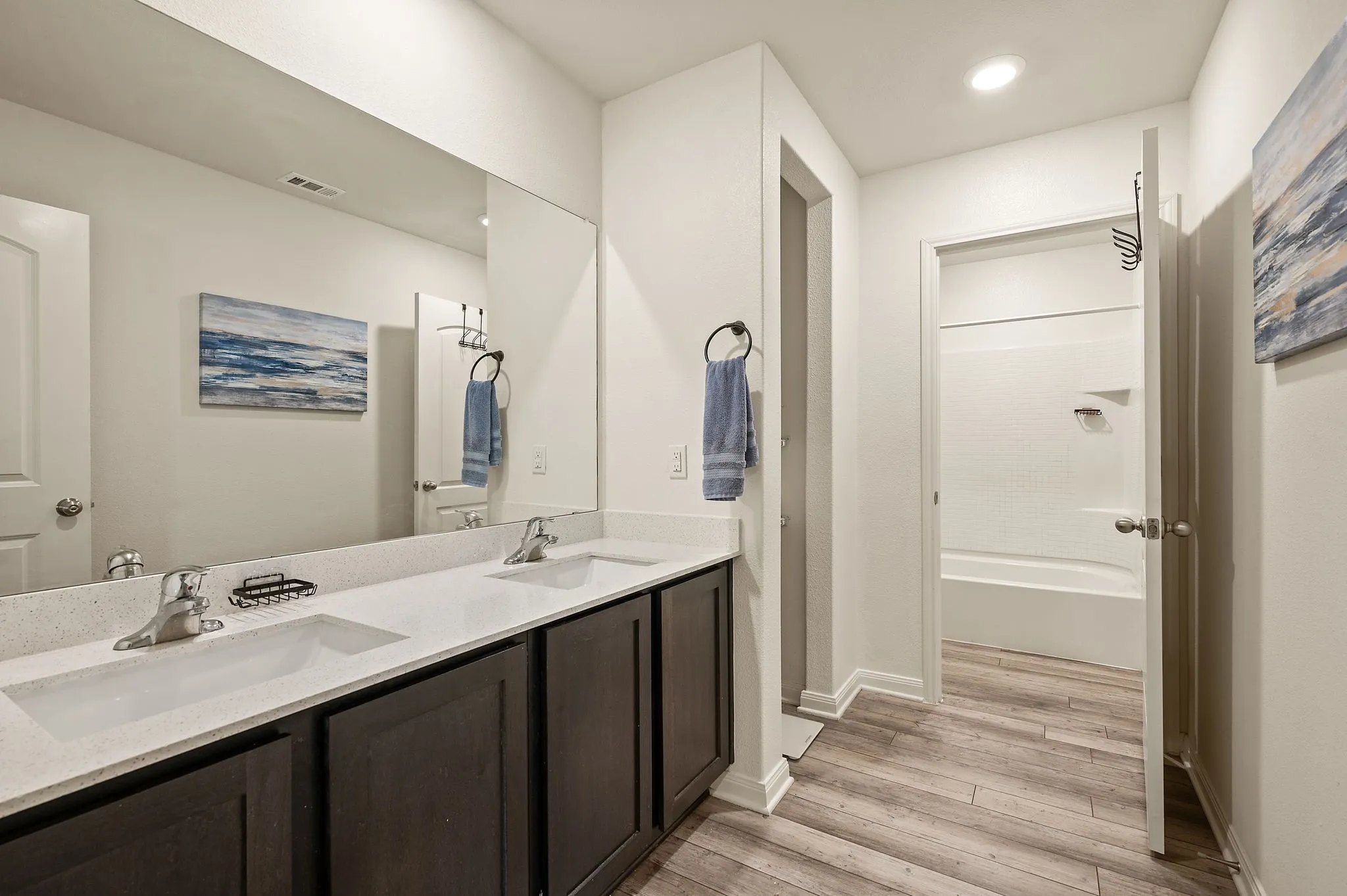 Dual vanity with undermount sinks, expansive wall-mounted mirror, dark wood-finish cabinetry, light wood-finish flooring, and recessed lighting