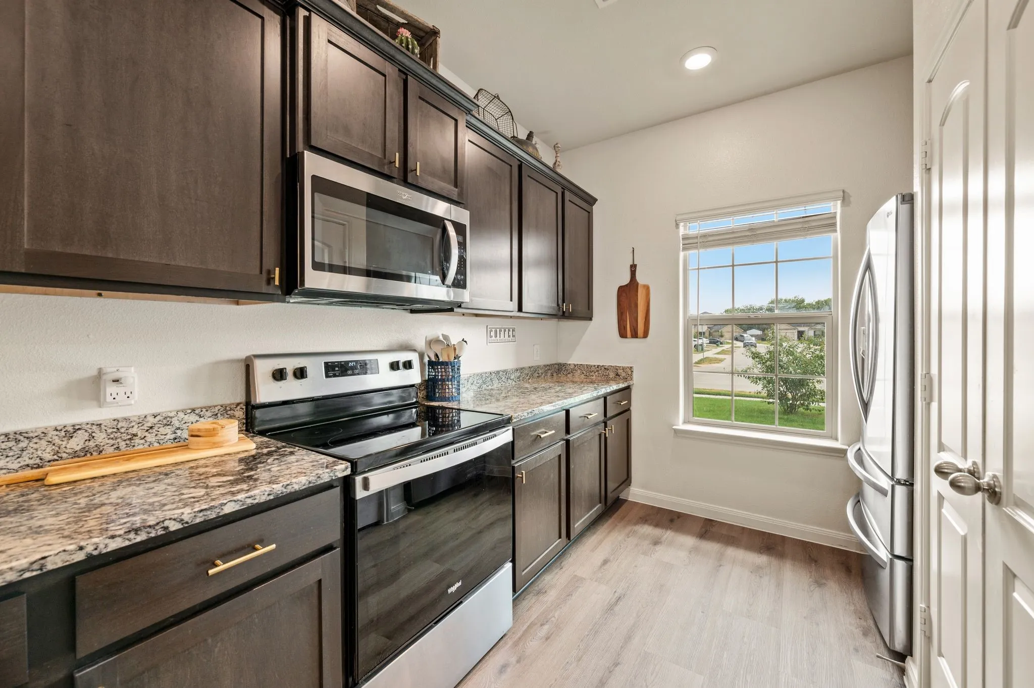 Kitchen featuring dark wood cabinetry, stainless steel appliances, speckled countertops, and wood-finish flooring