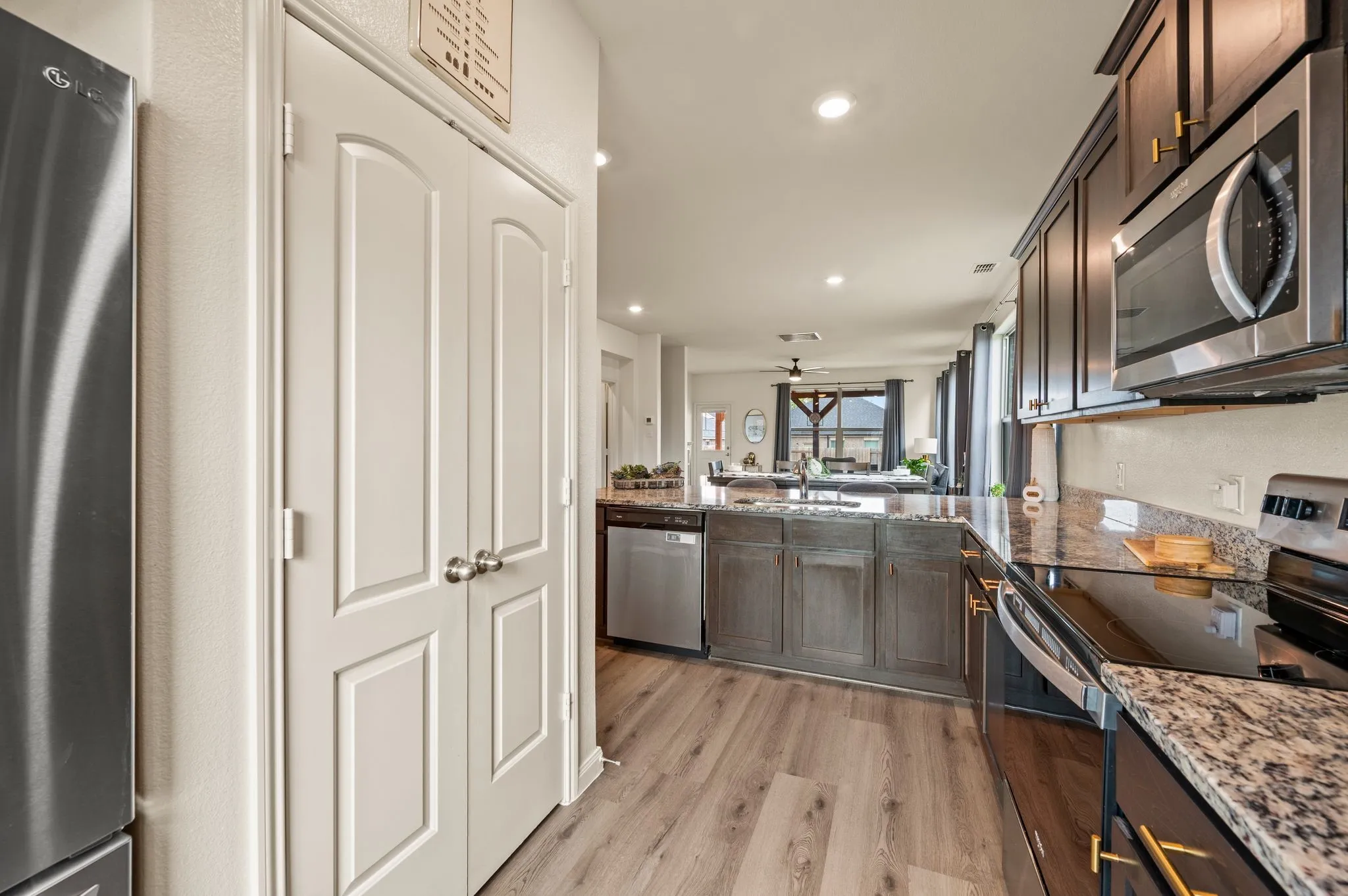 Kitchen featuring a stainless steel refrigerator, dark wood finish cabinetry, stainless steel microwave, black cooktop, and granite countertops