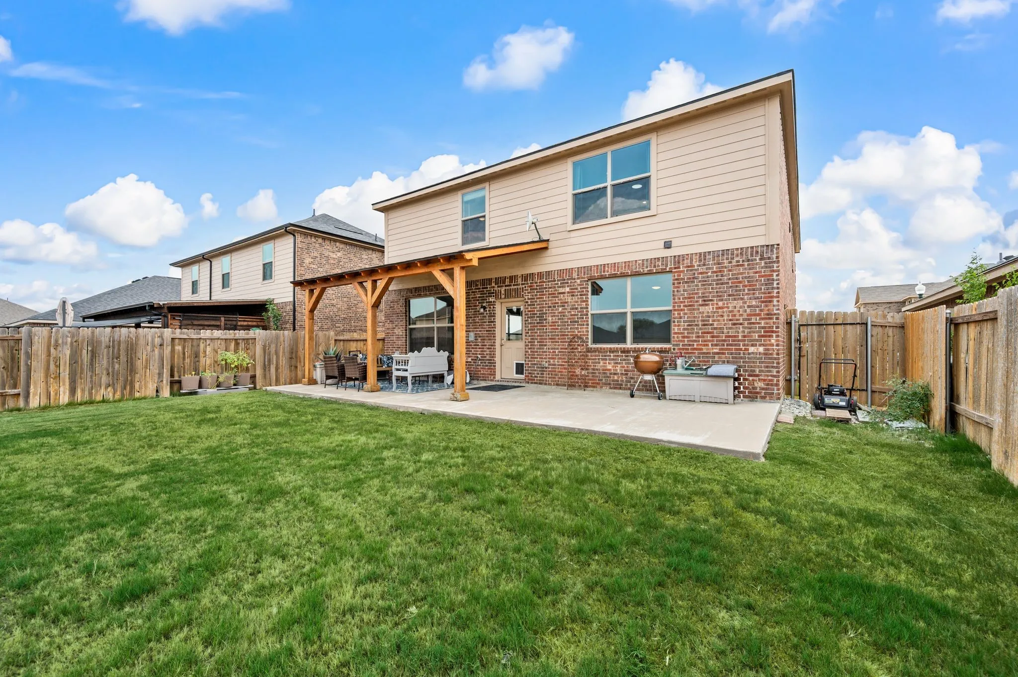 Expansive backyard featuring a manicured lawn, full wood fencing, and a concrete patio with a wood pergola