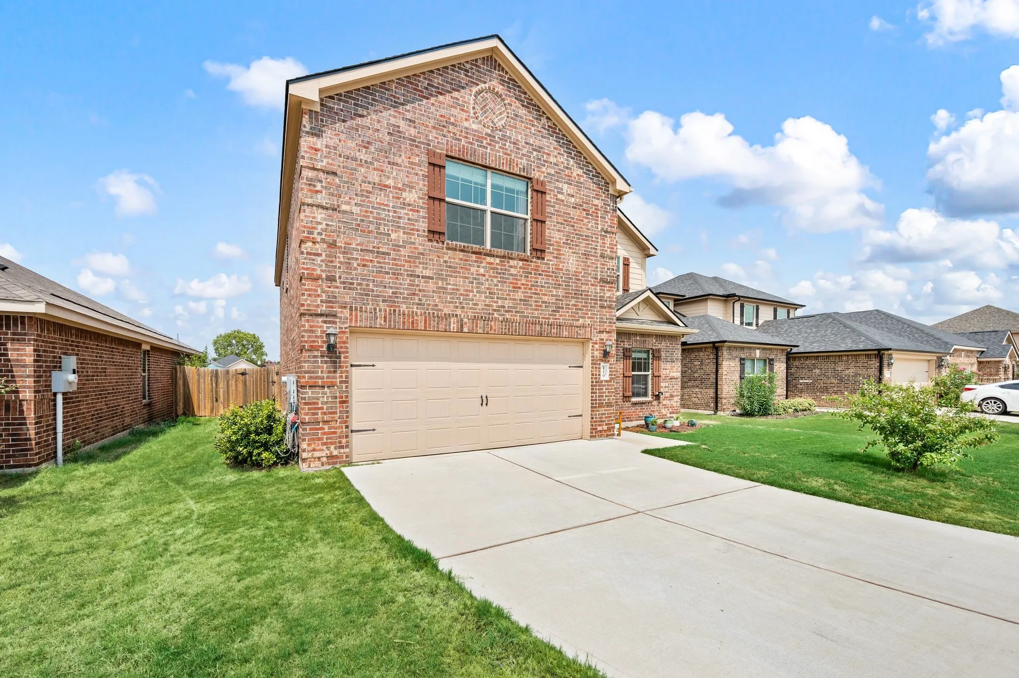 Brick facade with decorative wood shutters, two-car garage, concrete driveway, and a landscaped front yard