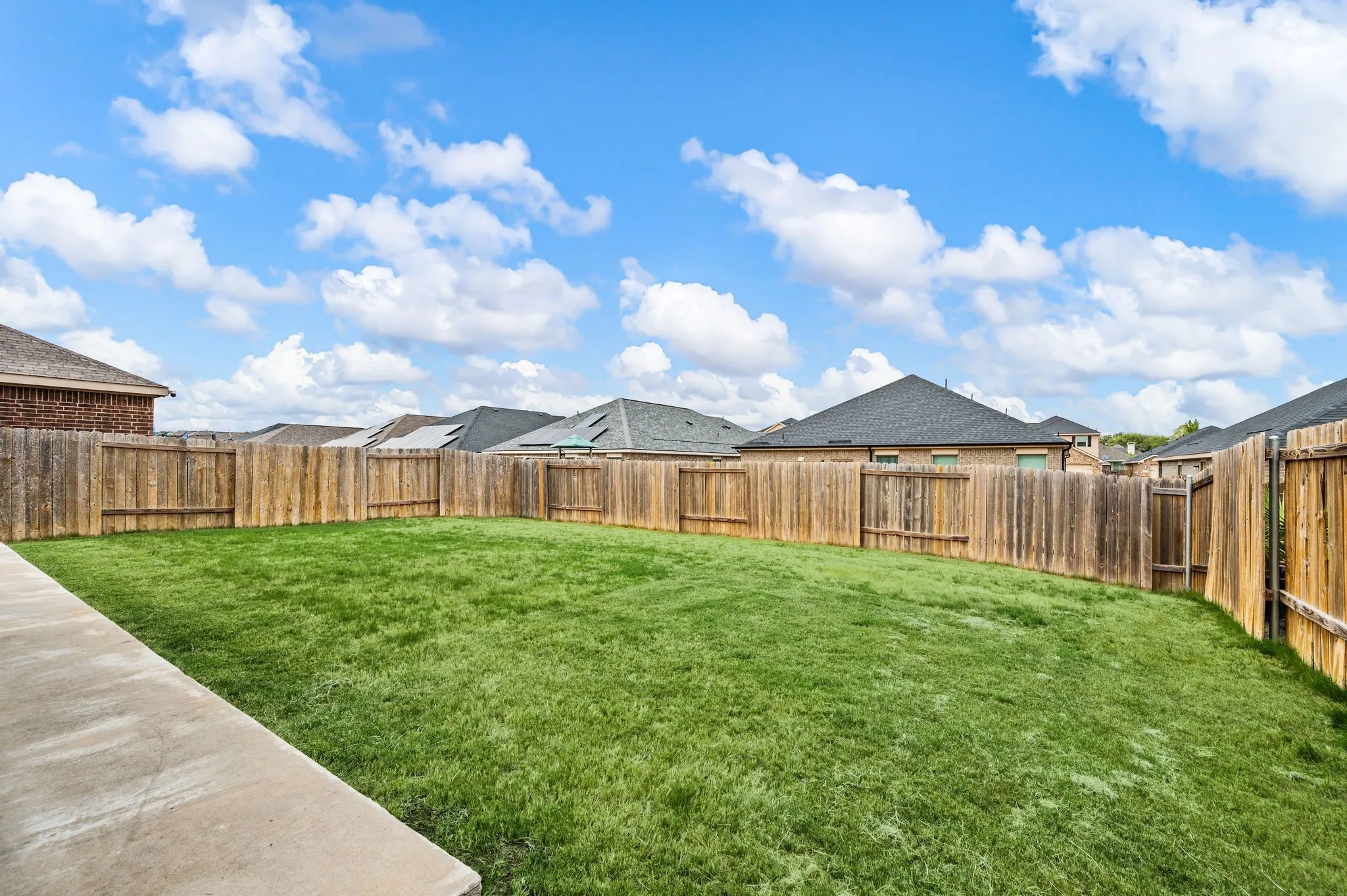 Expansive backyard featuring a manicured lawn, full wood fencing, and a concrete pathway