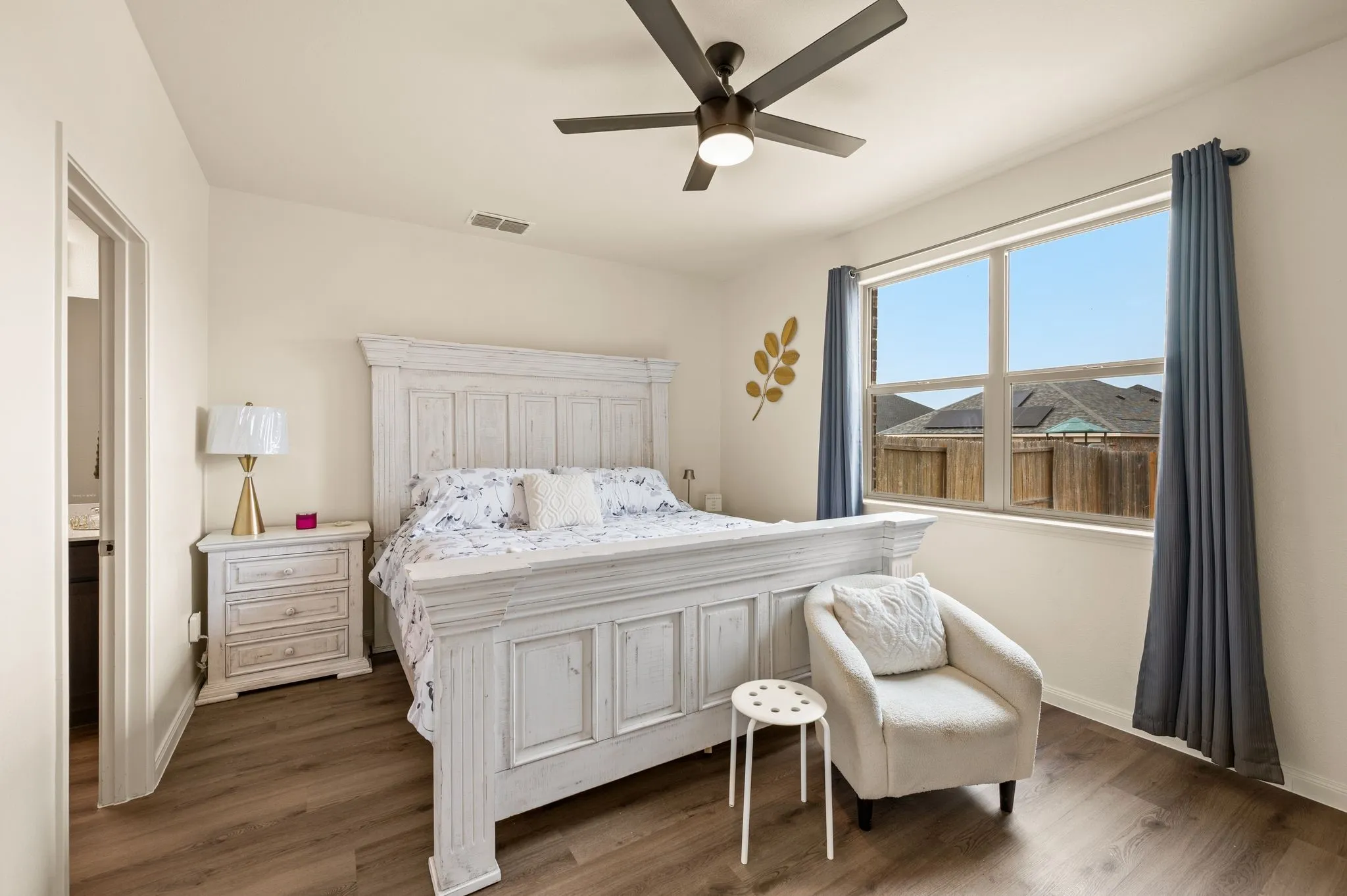 Wood-finish flooring, ceiling fan with integrated lighting, and a large window with privacy fencing visible
