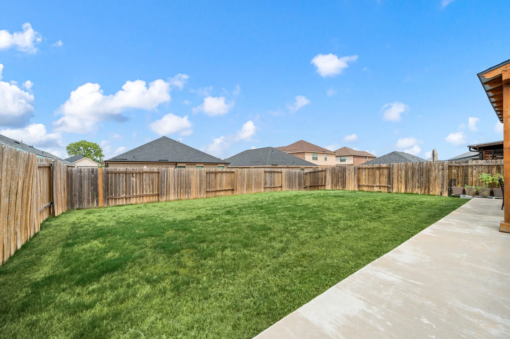 Expansive backyard with a manicured lawn, full wood fencing, and a concrete patio