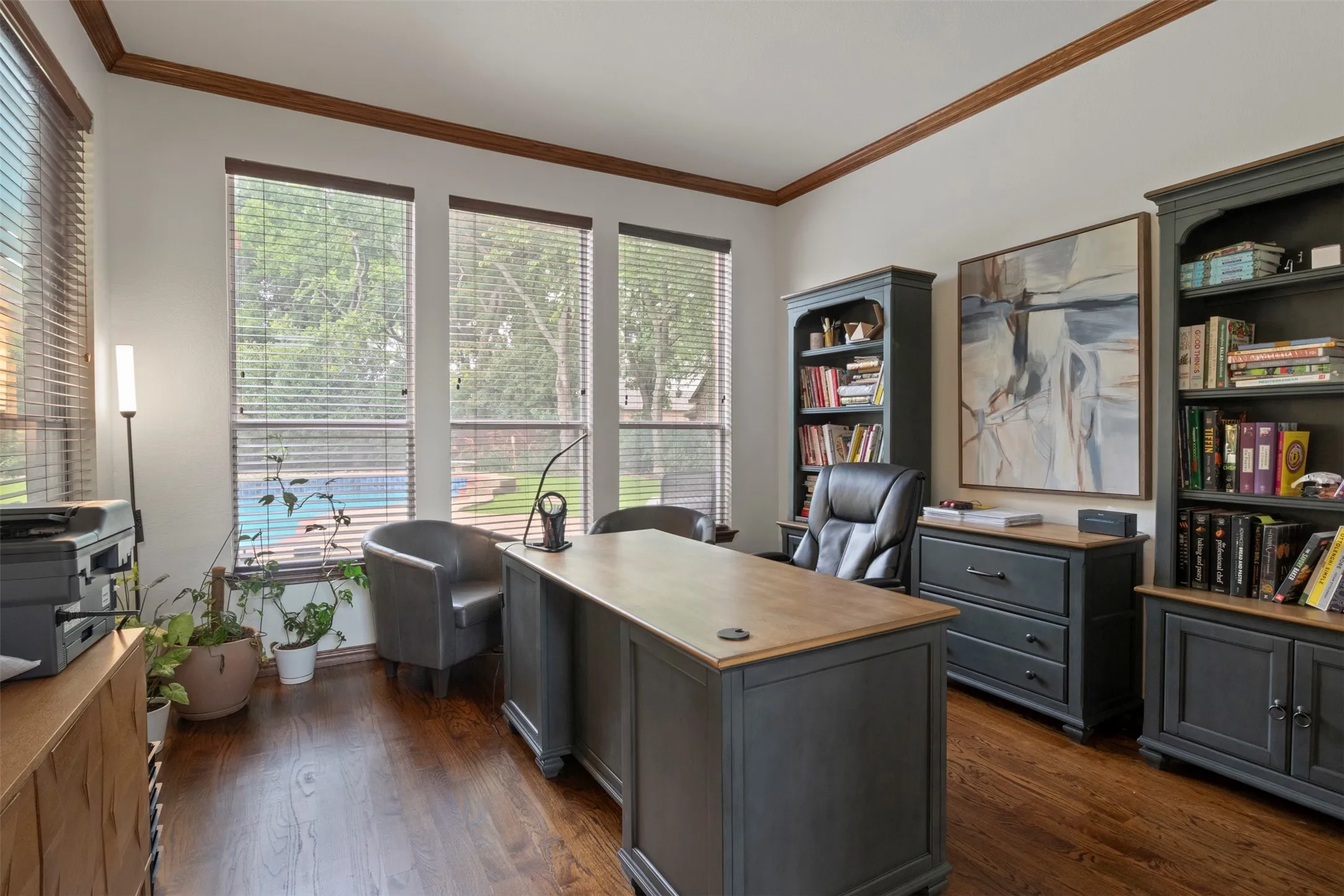 Hardwood flooring, crown molding, built-in shelving, built-in cabinetry, and large windows with outdoor pool visible