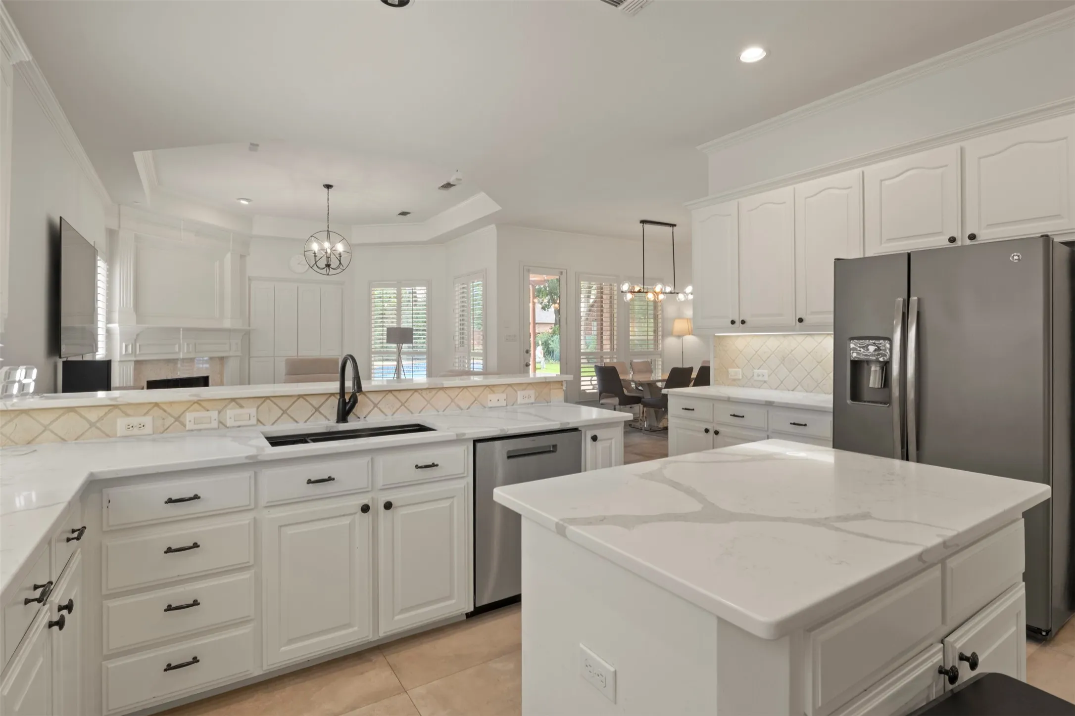 White cabinetry with black hardware, white countertops, tile backsplash, built-in stainless steel appliances, and a central island