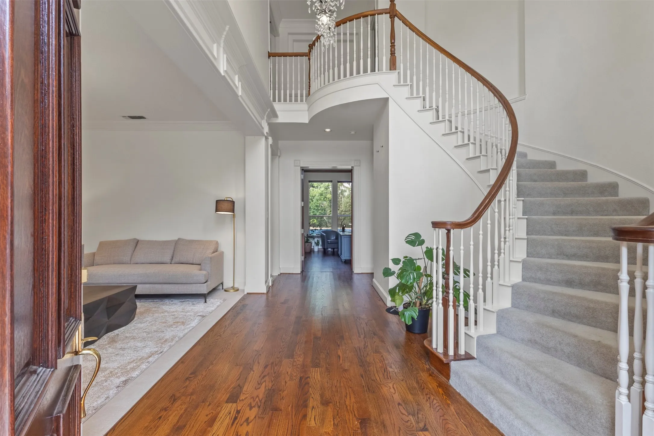 Wood-finish flooring with a curved staircase featuring carpeted treads, white balusters, and a rich wood handrail