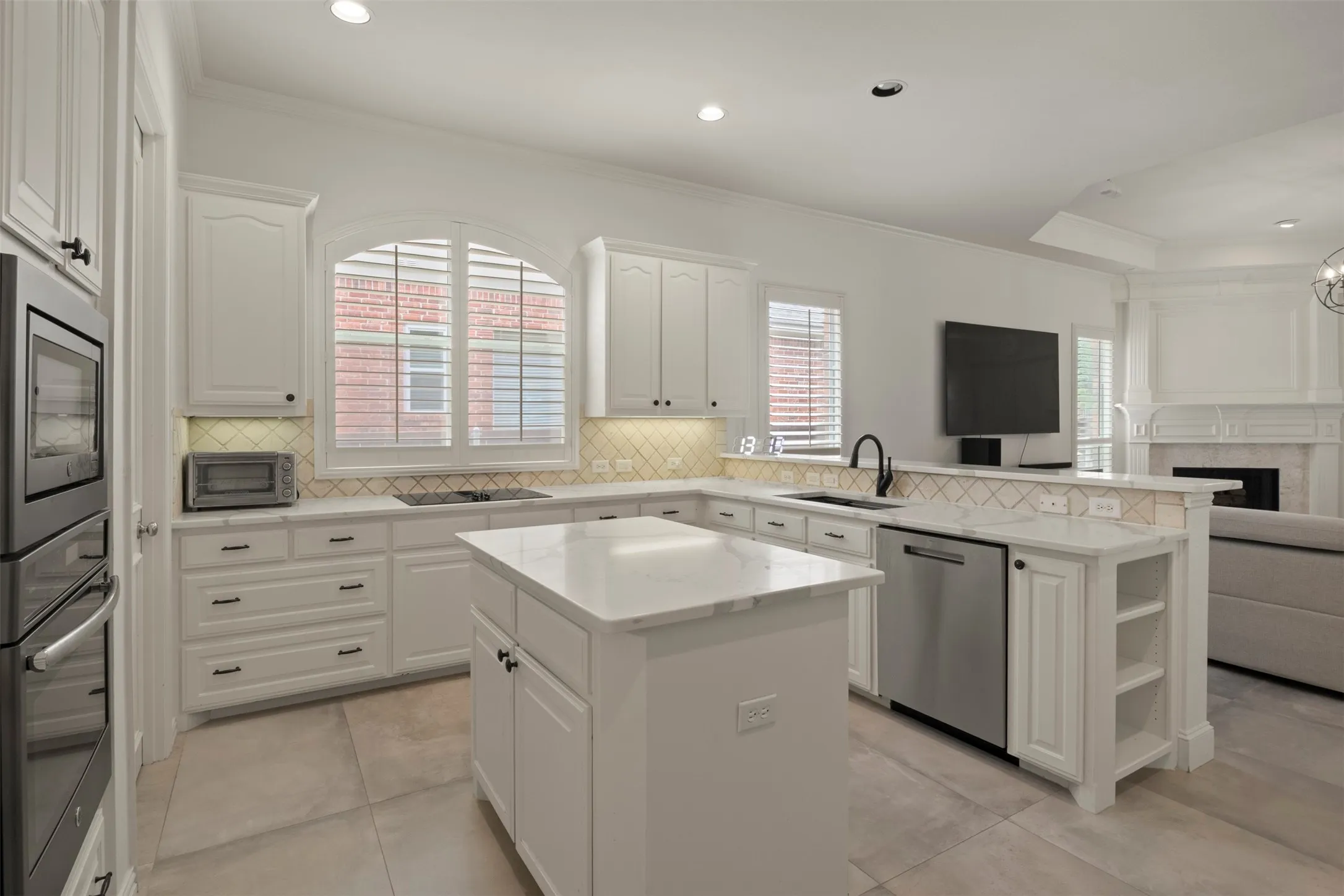 White cabinetry with dark hardware, a center island with a stone countertop, built-in double oven, integrated dishwasher, and a tile backsplash