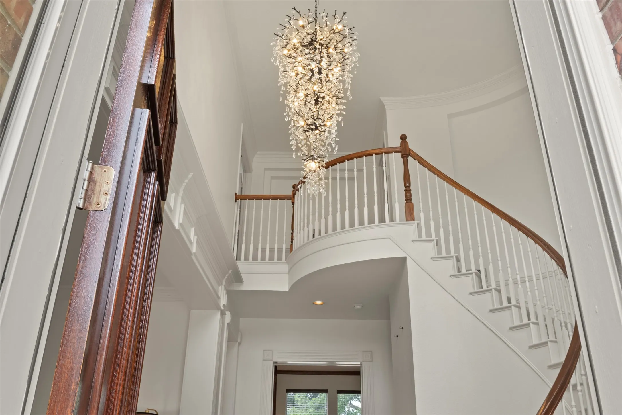 Stunning two-story foyer showcasing a curved staircase with wood-finish railings and white balusters, accented by a dramatic crystal chandelier suspended from the ceiling
