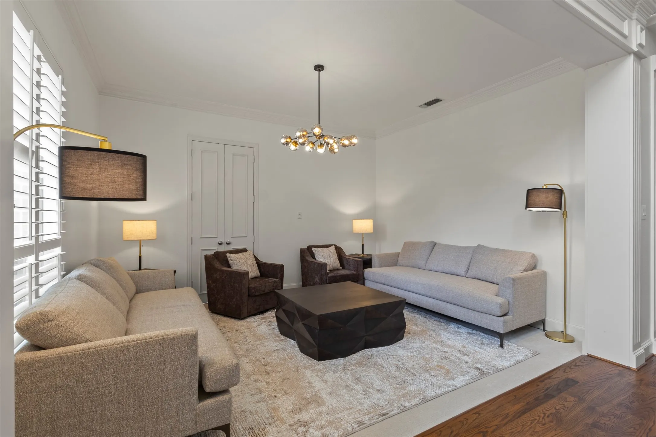 Spacious living area featuring high ceilings, crown molding, a contemporary chandelier, and plantation shutters