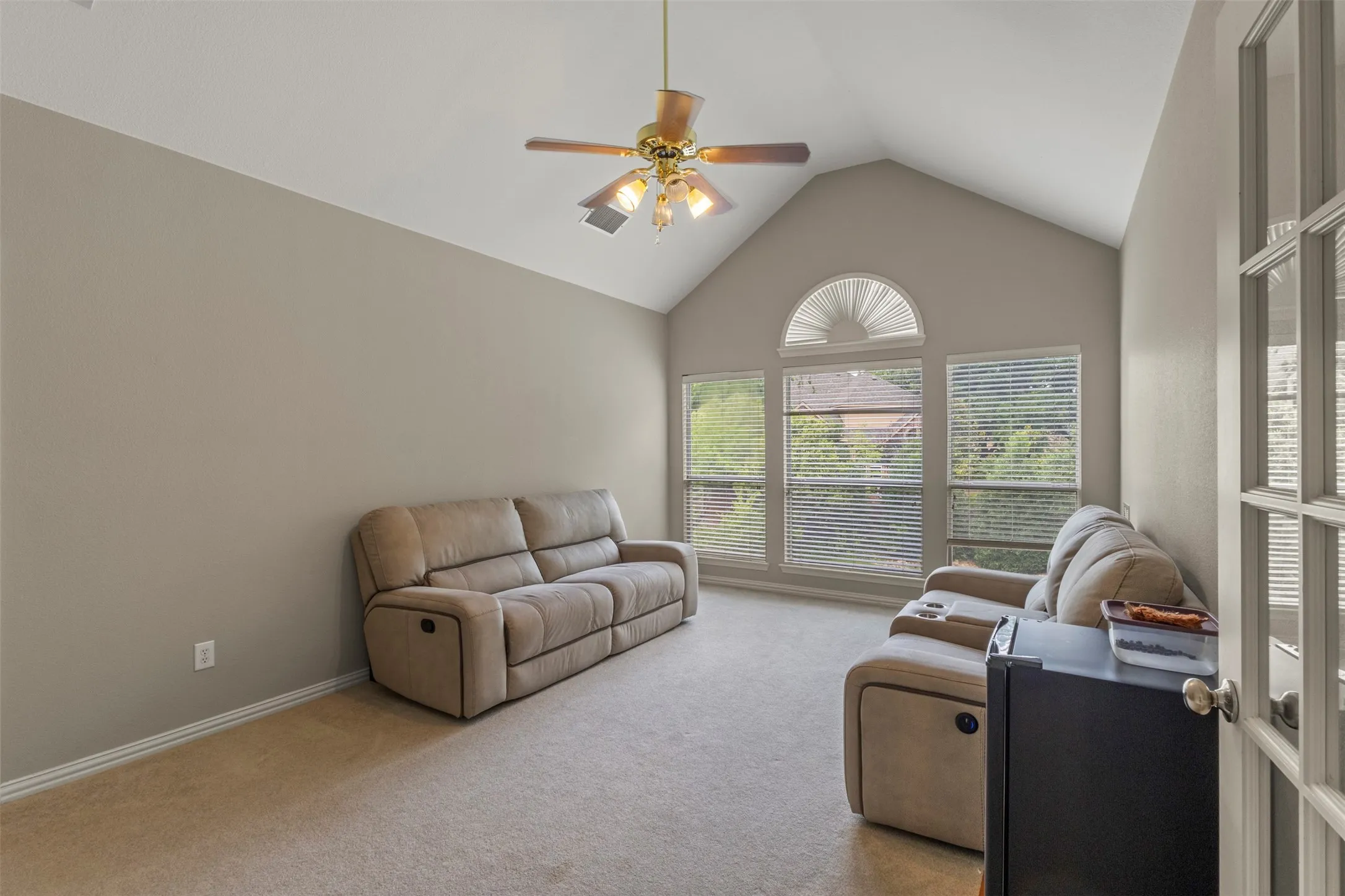 Vaulted ceiling with an illuminated ceiling fan, a series of windows, and a glass-paneled door