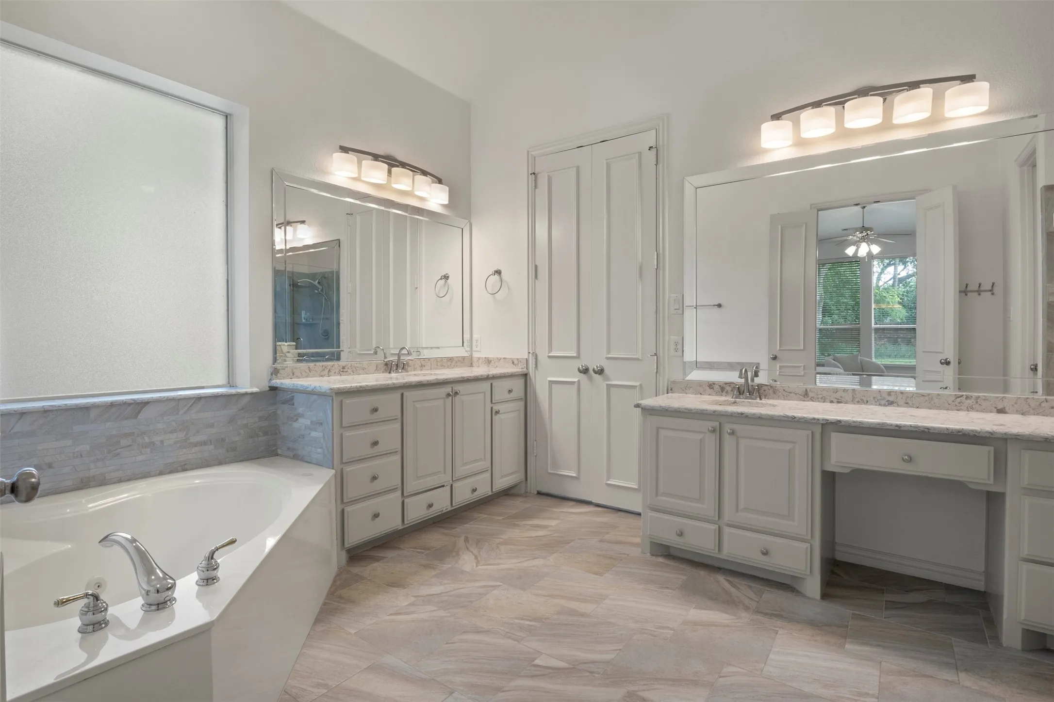 Dual vanities with integrated sinks and white cabinetry, a built-in soaking tub with chrome fixtures, and wood-finish flooring