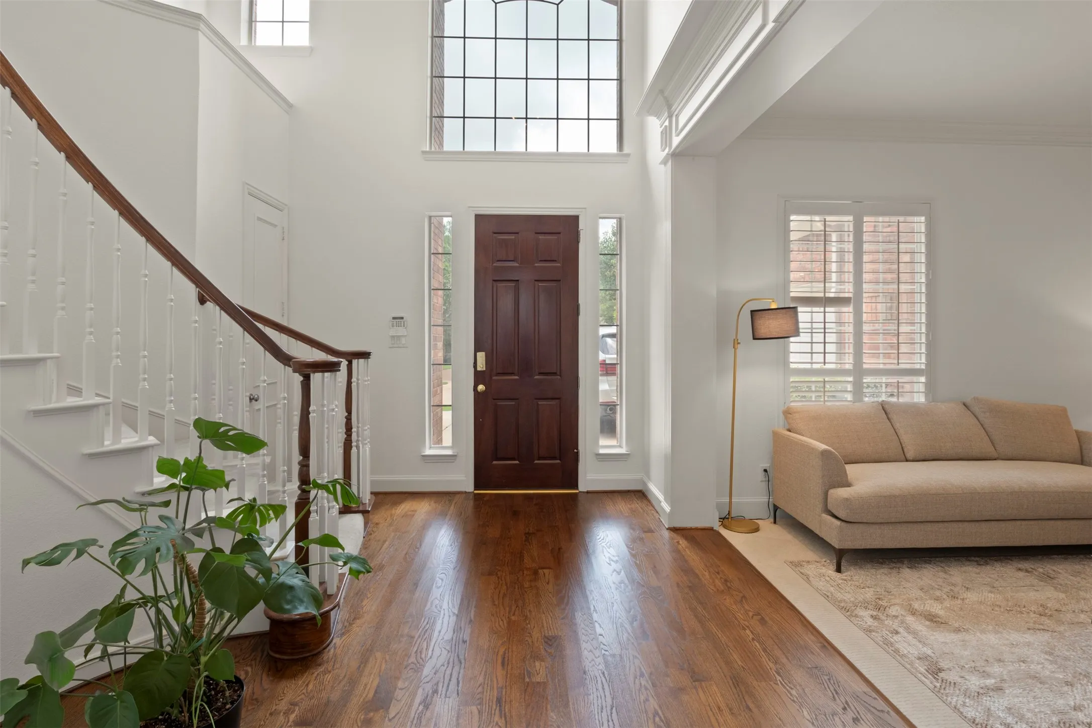 Two-story entry with hardwood flooring, a multi-pane arched window, and a grand staircase featuring a wood handrail