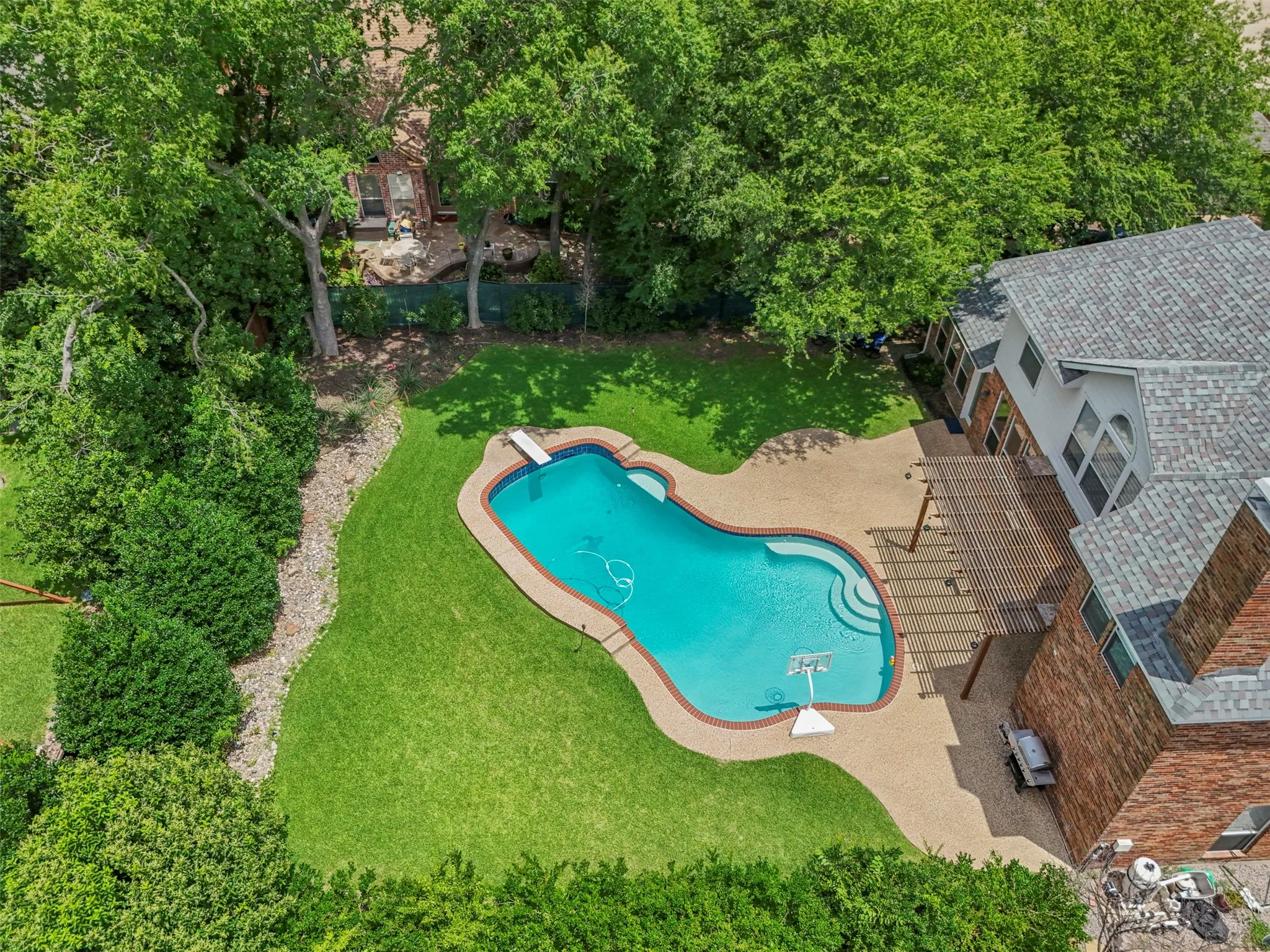 Spacious backyard featuring a freeform swimming pool, extensive patio, and a wooden pergola structure