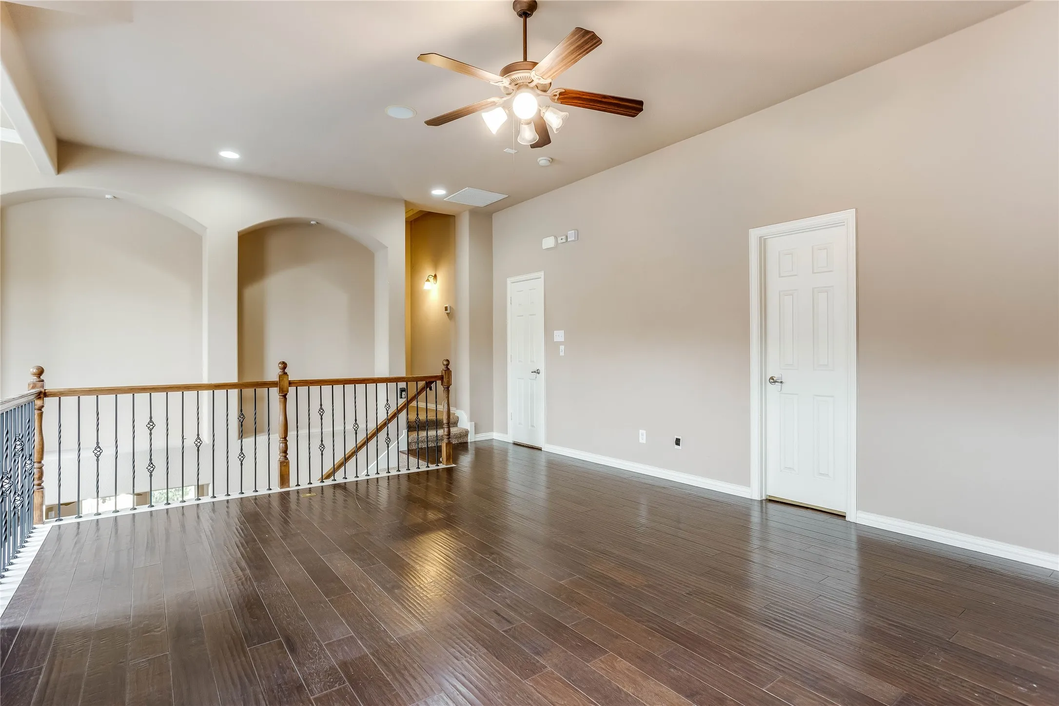Expansive room featuring wood-finish flooring, a ceiling fan with integrated lighting, recessed lighting, and a wrought iron and wood railing