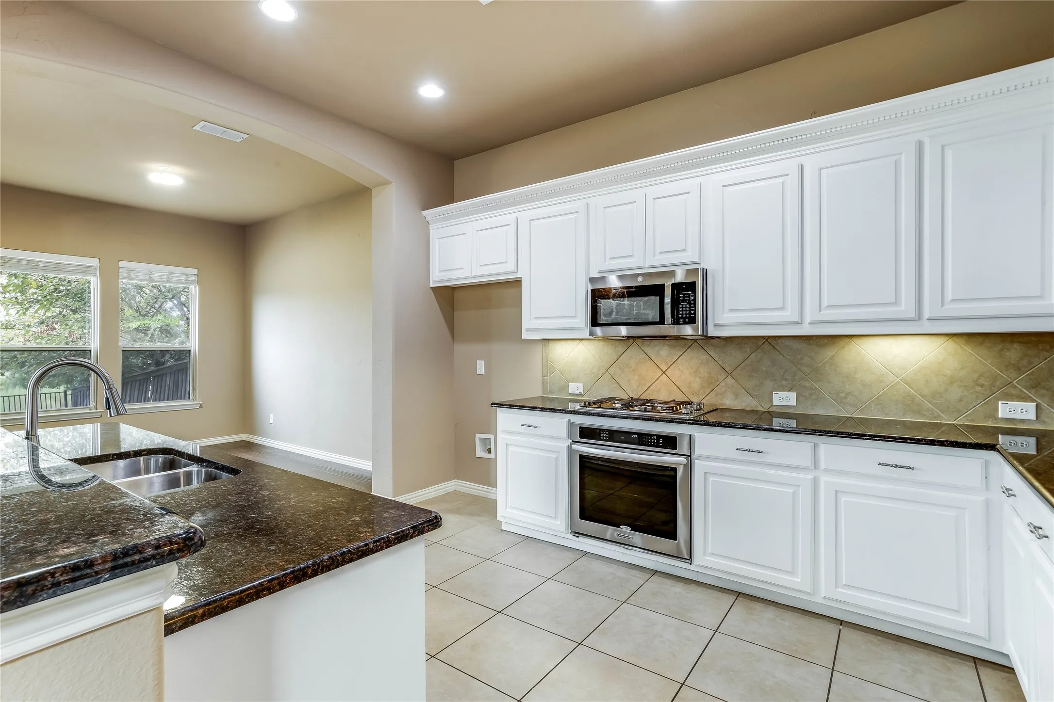 Kitchen featuring white cabinetry, dark stone countertops, stainless steel appliances, tile flooring, and a tile backsplash