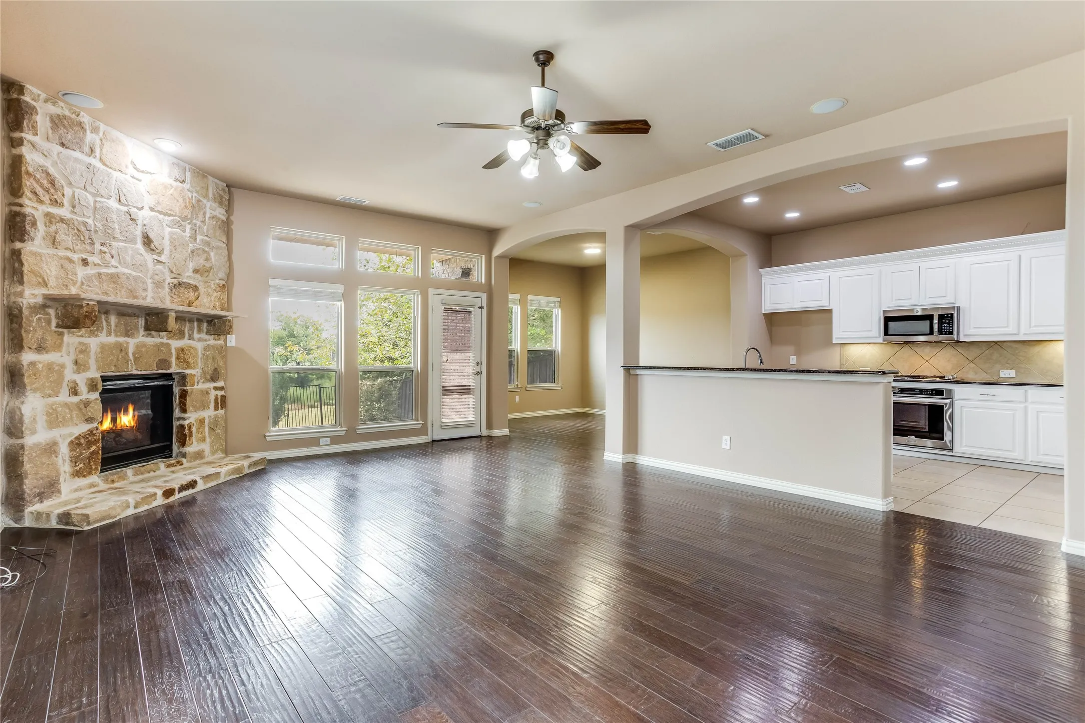 Spacious living area featuring wood-finish flooring, a stone fireplace, and a ceiling fan