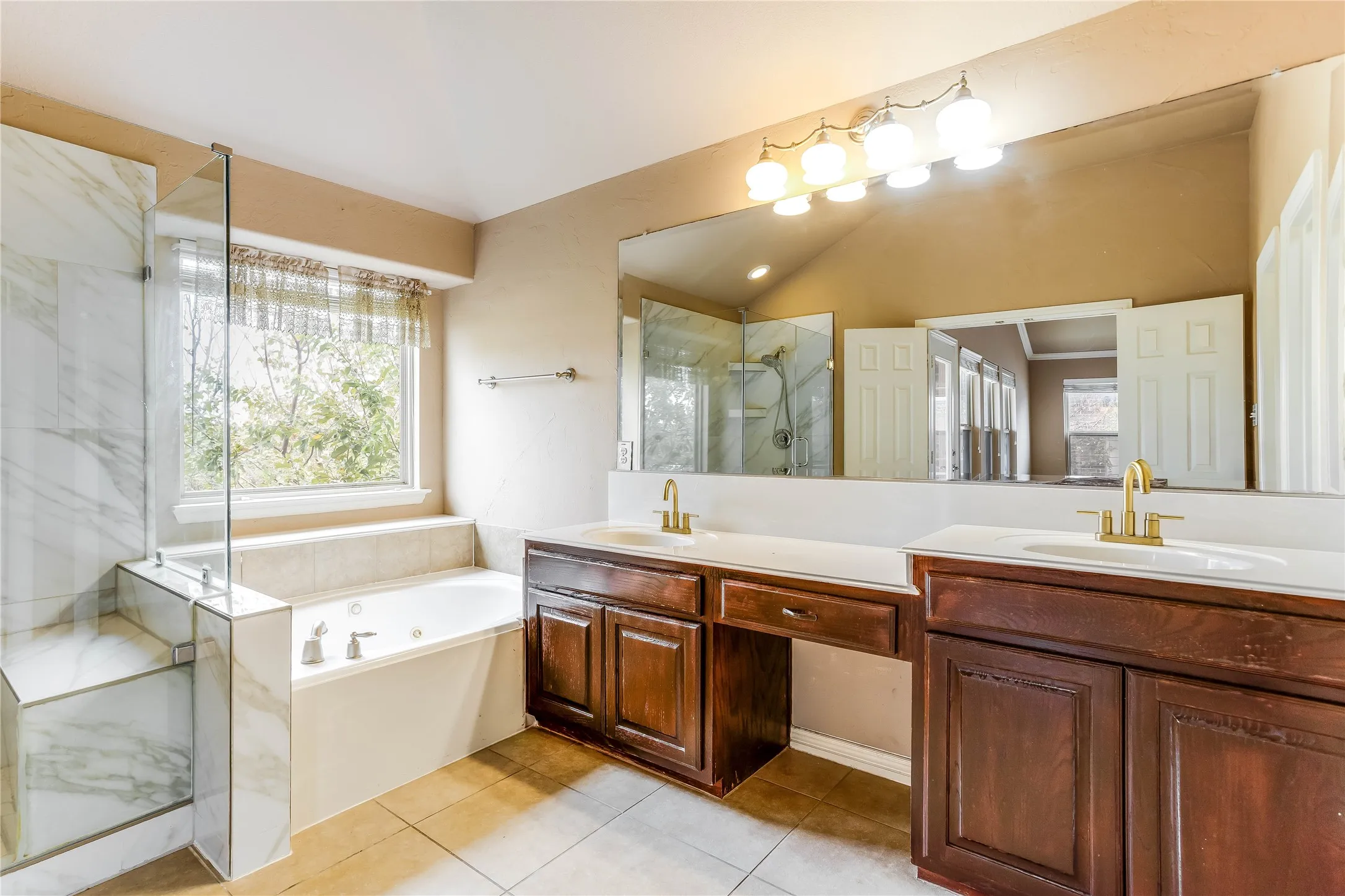 Built-in soaking tub, separate glass-enclosed shower with tile surround, dual vanity with undermount sinks, and wood-finish cabinetry