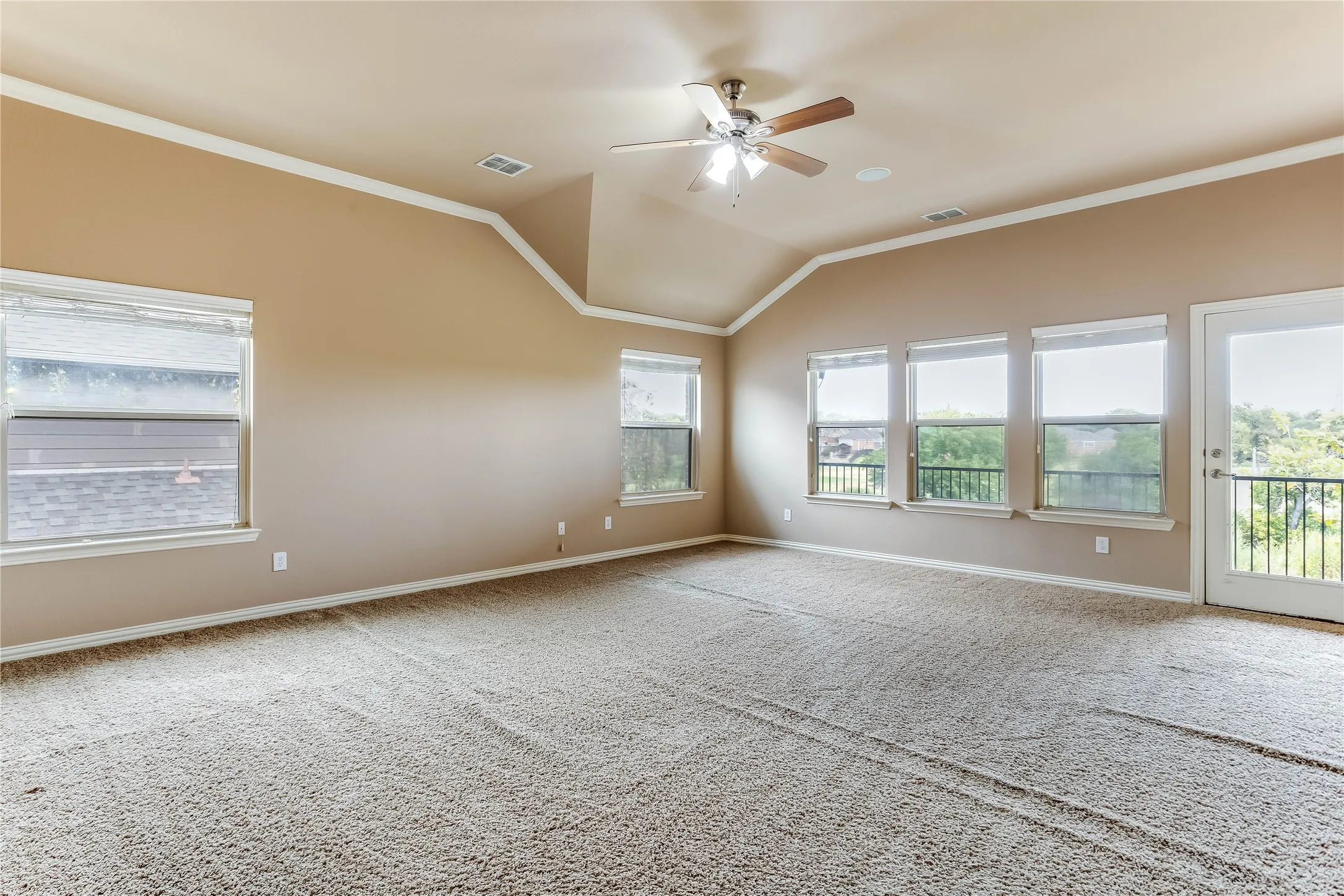 Vaulted ceiling with crown molding, ceiling fan, and multiple windows
