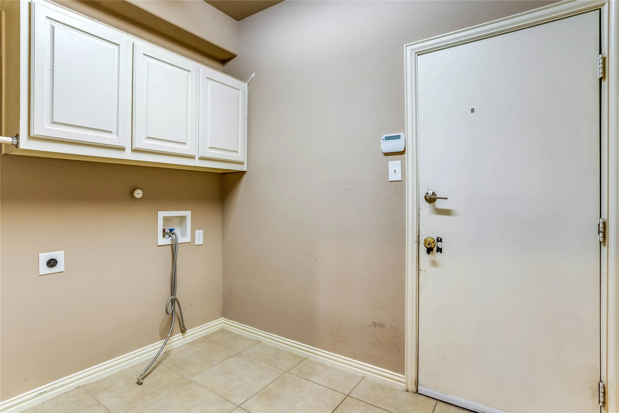White shaker-style cabinetry with overhead storage, tile flooring, and utility hookups