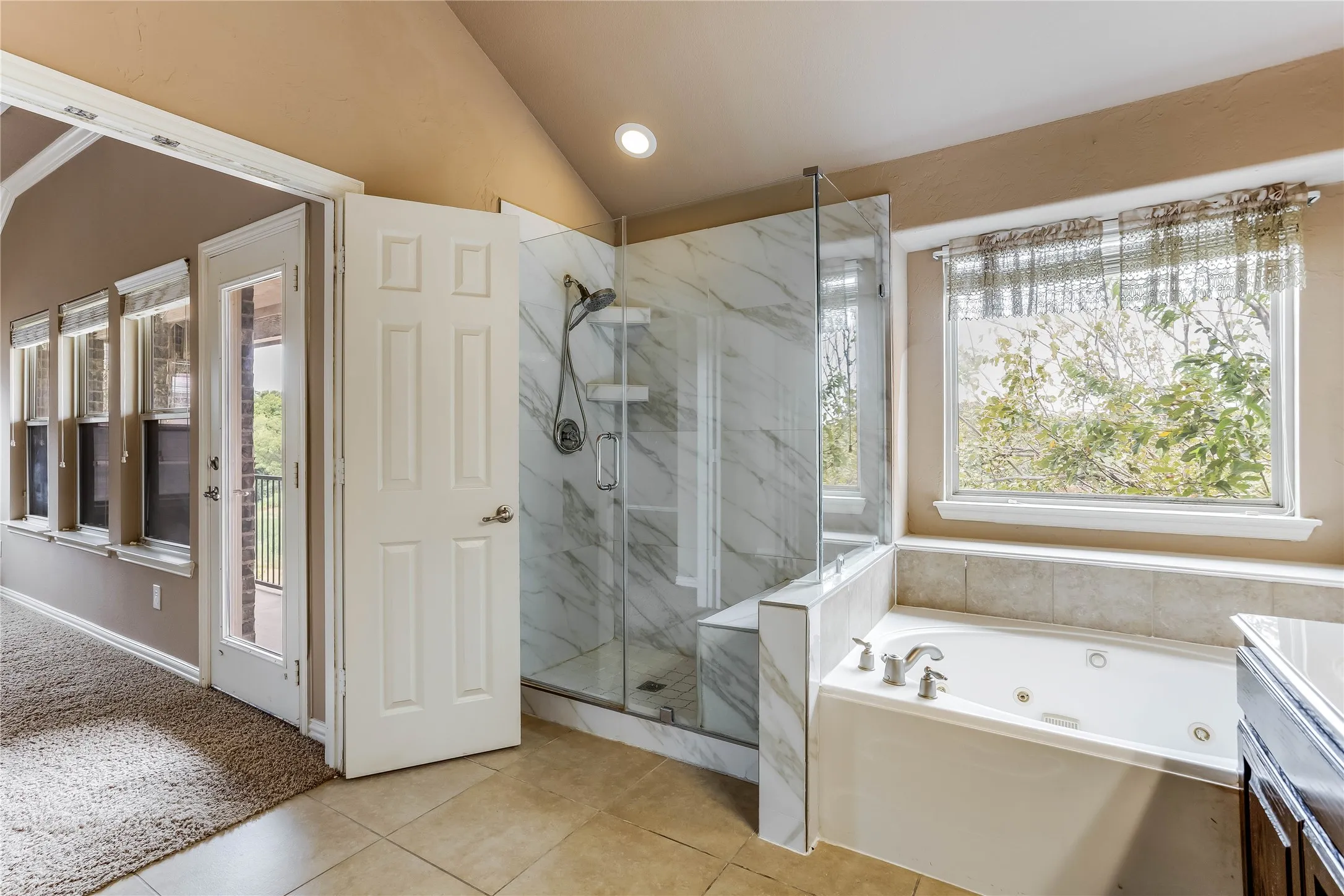 Glass-enclosed shower with marble-finish tile, a built-in bench, and an adjacent jetted soaking tub