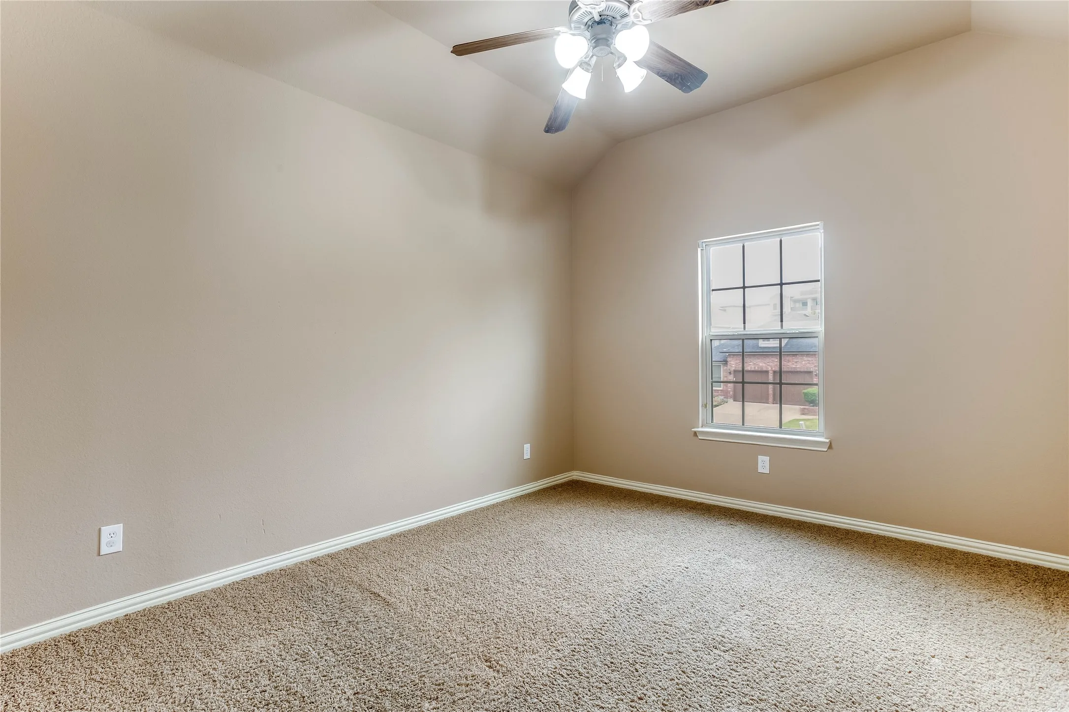 Vaulted ceiling, ceiling fan, single window with grid pattern, neutral-toned walls, and carpet flooring