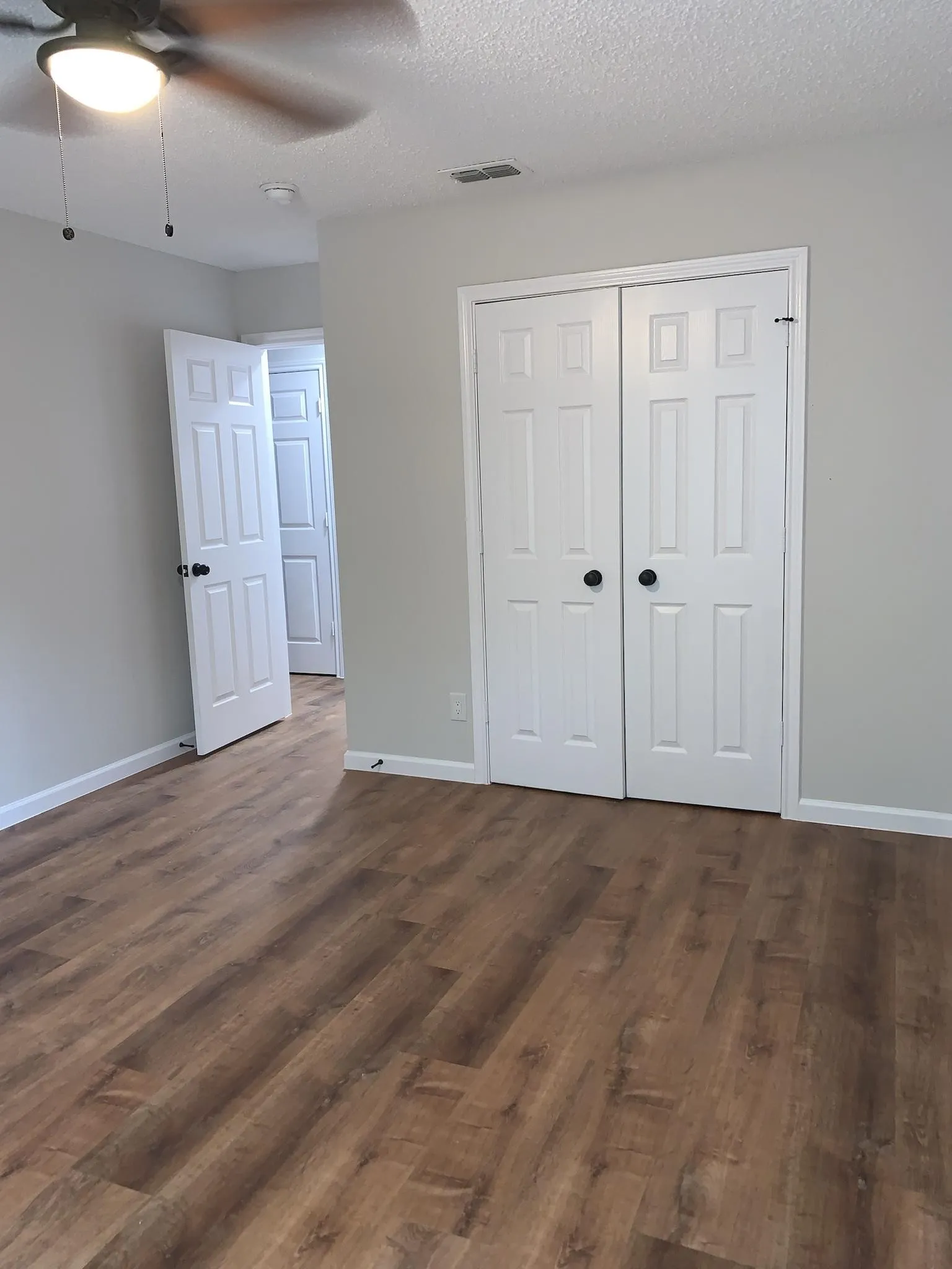 Wood-finish flooring, white paneled doors with black hardware, and a ceiling fan with integrated lighting