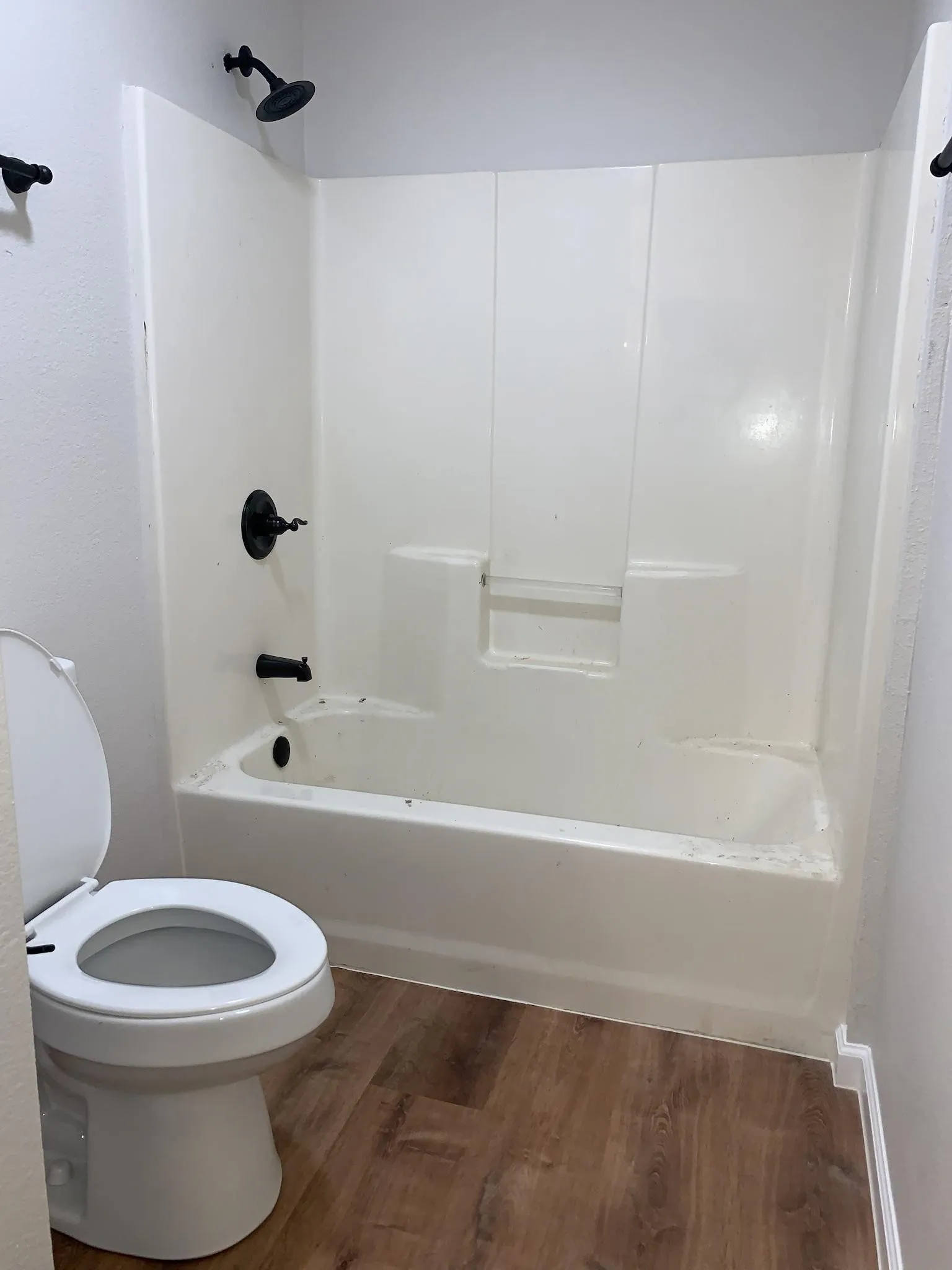 White toilet with a coordinated shower and tub combination featuring matte black fixtures, set on wood-finish flooring