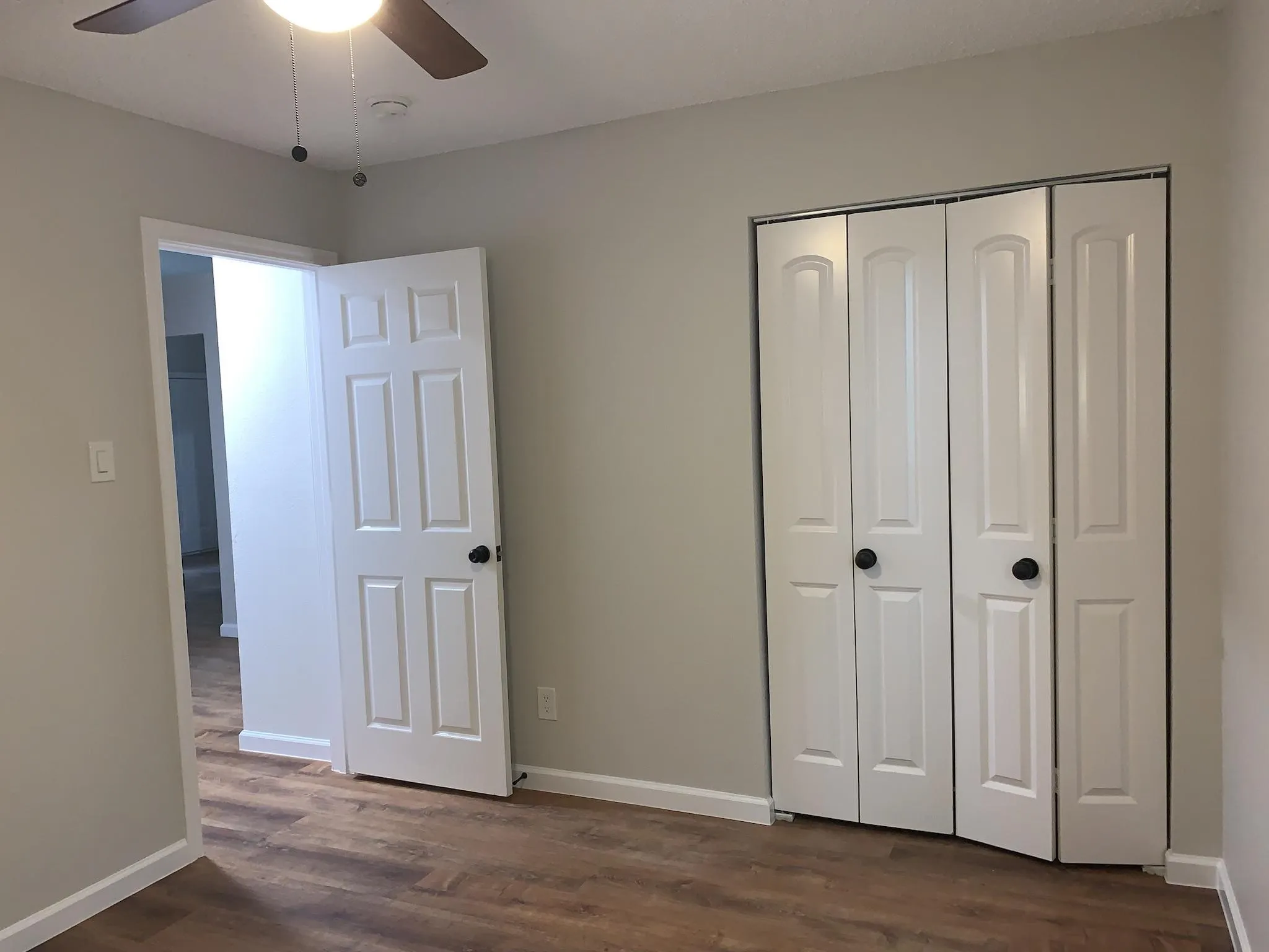 Wood-finish flooring, ceiling fan with integrated lighting, white paneled doors, and bi-fold closet doors with black hardware