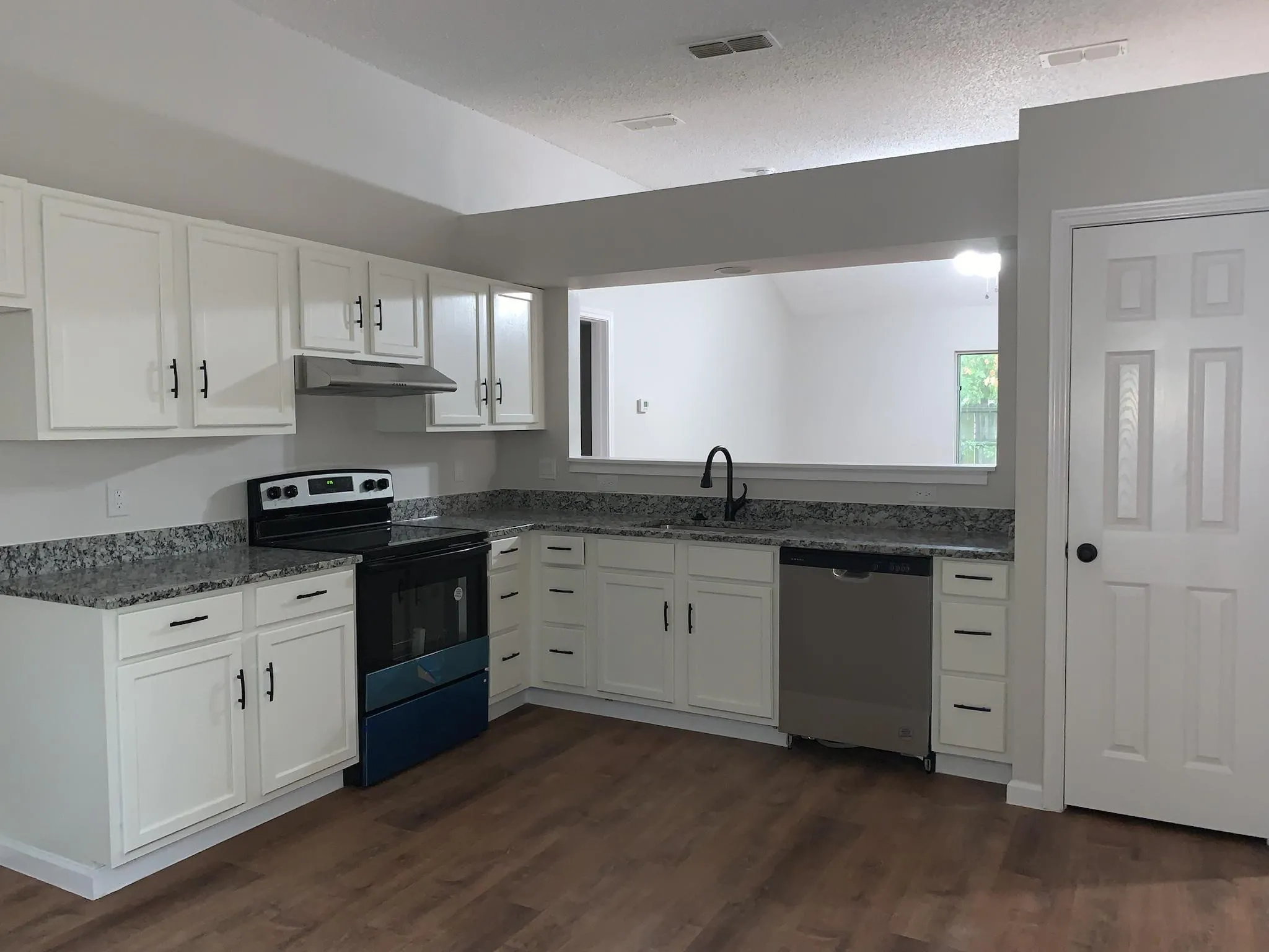 Kitchen featuring wood-finish flooring, white cabinetry with black hardware, granite-look countertops, and stainless steel appliances