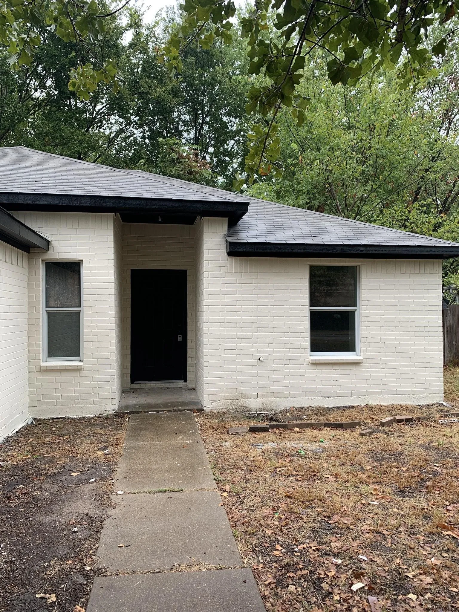 Brick exterior with a white finish, dark roof shingles, and a concrete walkway