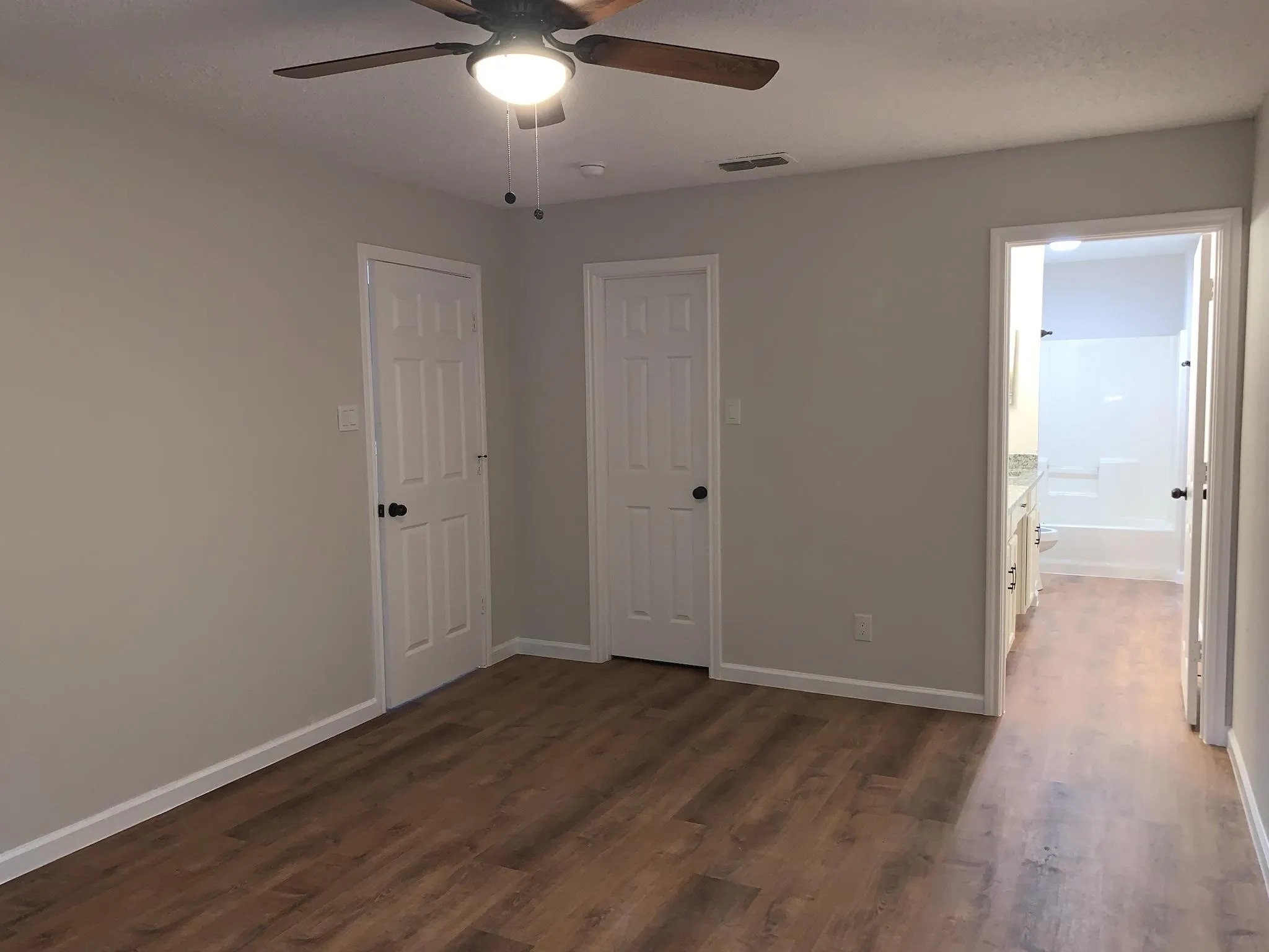 Wood-finish flooring, ceiling fan with integrated lighting, paneled doors, and light-toned walls
