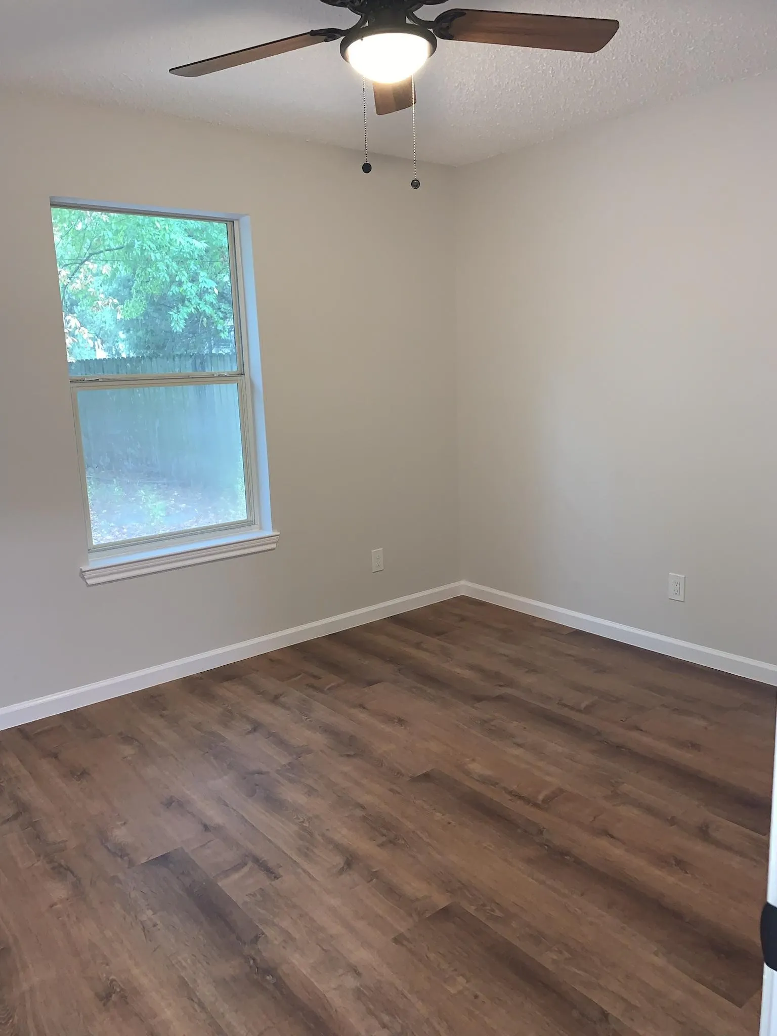 Wood-finish flooring with white trim, a double-hung window, and a ceiling fan with integrated lighting