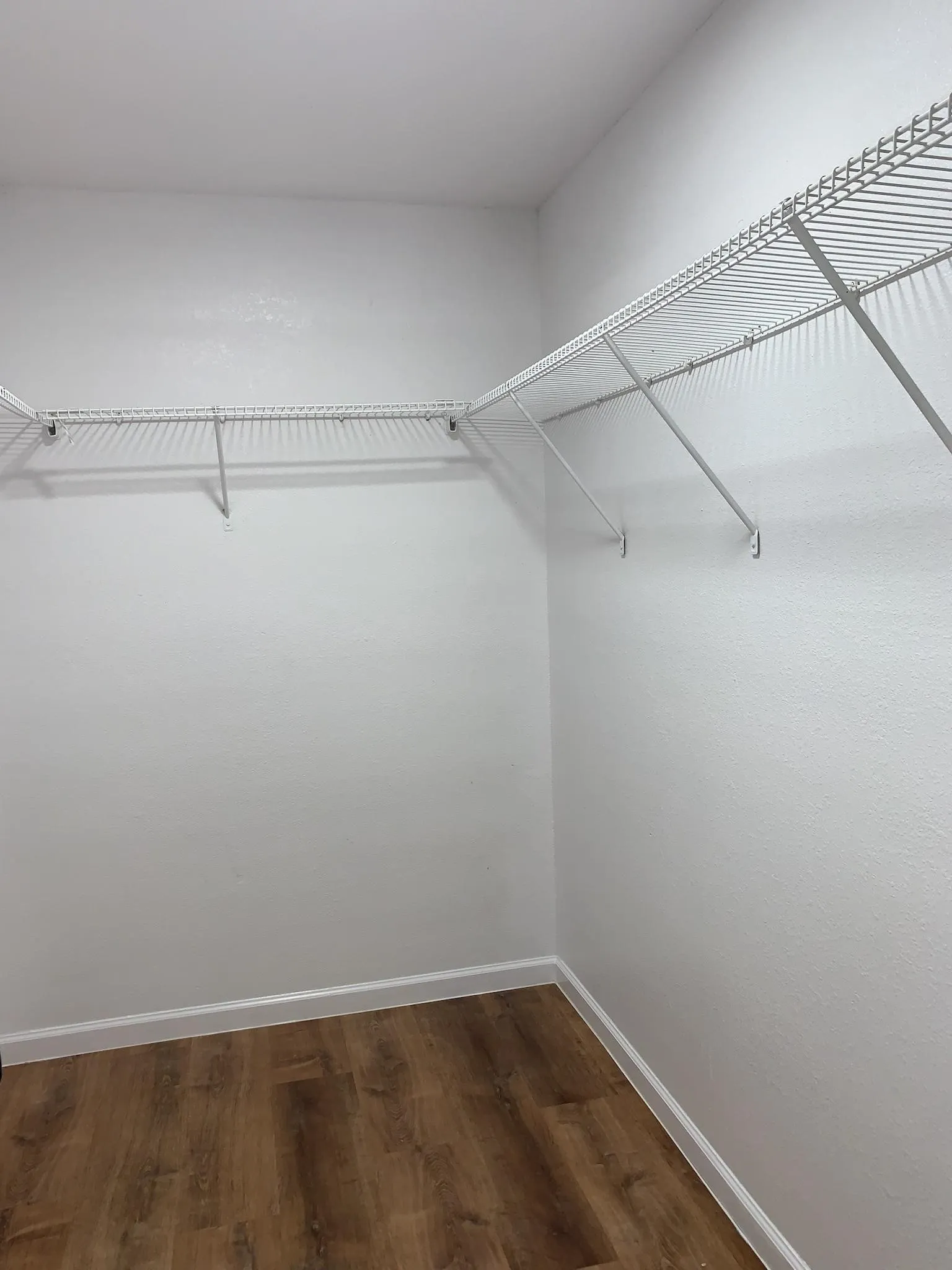 Wire shelving system with a corner configuration, white wall finish, and wood-finish flooring