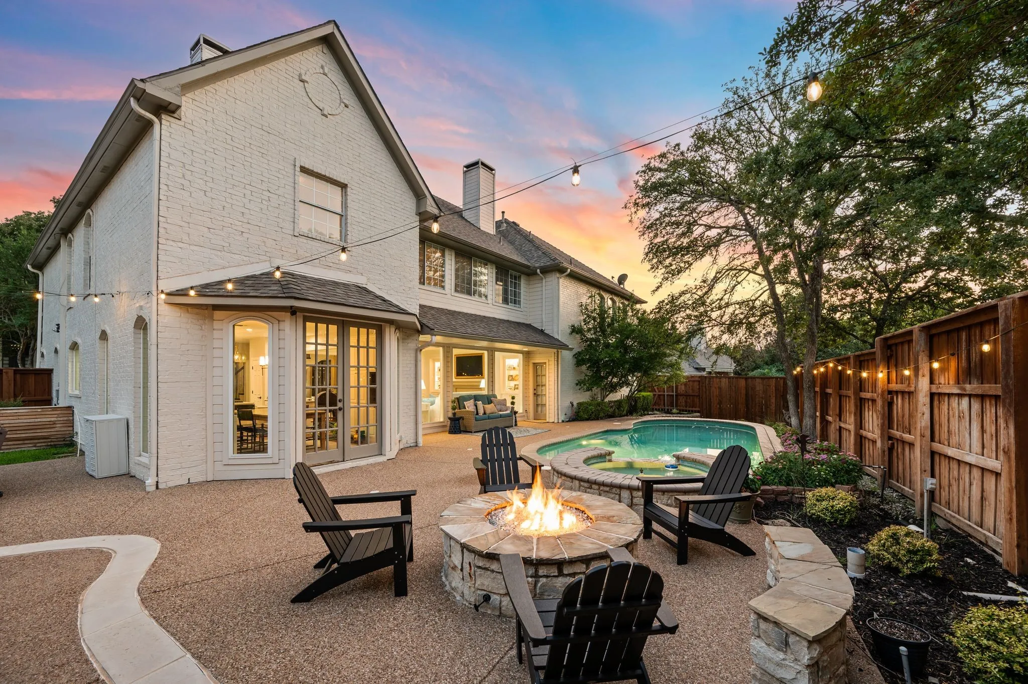 The fire pit becomes the center of the backyard after sunset, surrounded by the pool, trees and soft lighting throughout the property.