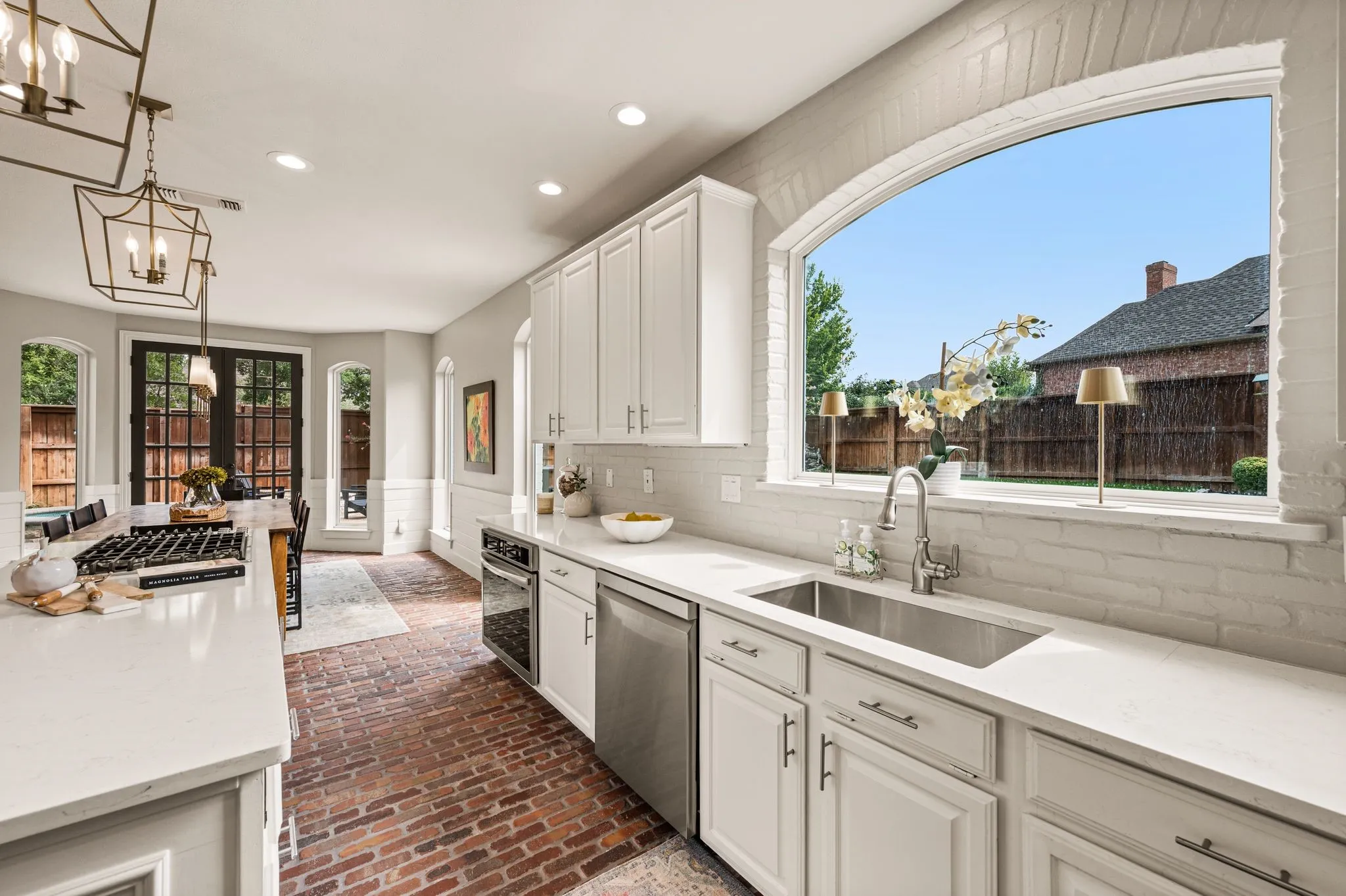 The sink is framed by a wide arched window, turning even the everyday spaces toward the backyard.