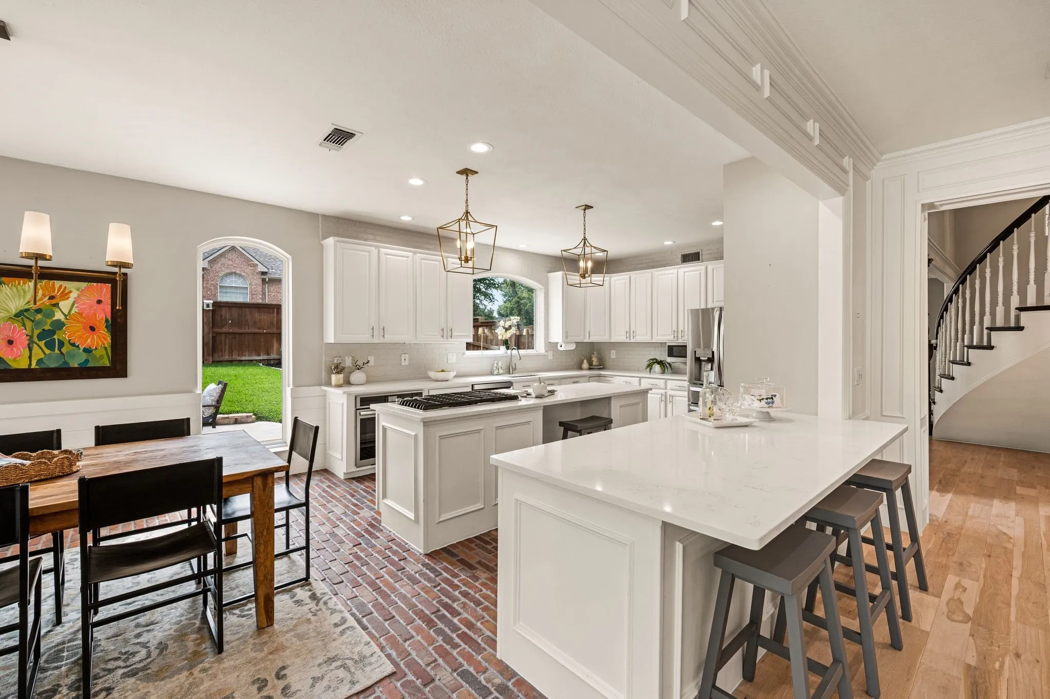 Two oversized islands create room for cooking, serving and gathering, while the brick floors bring character beneath the clean white cabinetry.