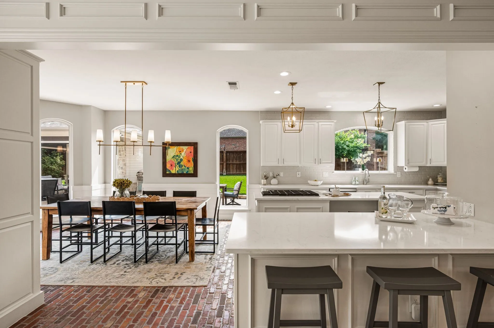 The kitchen opens generously to the breakfast room, where white cabinetry, brass lighting and brick floors give the space a collected warmth.