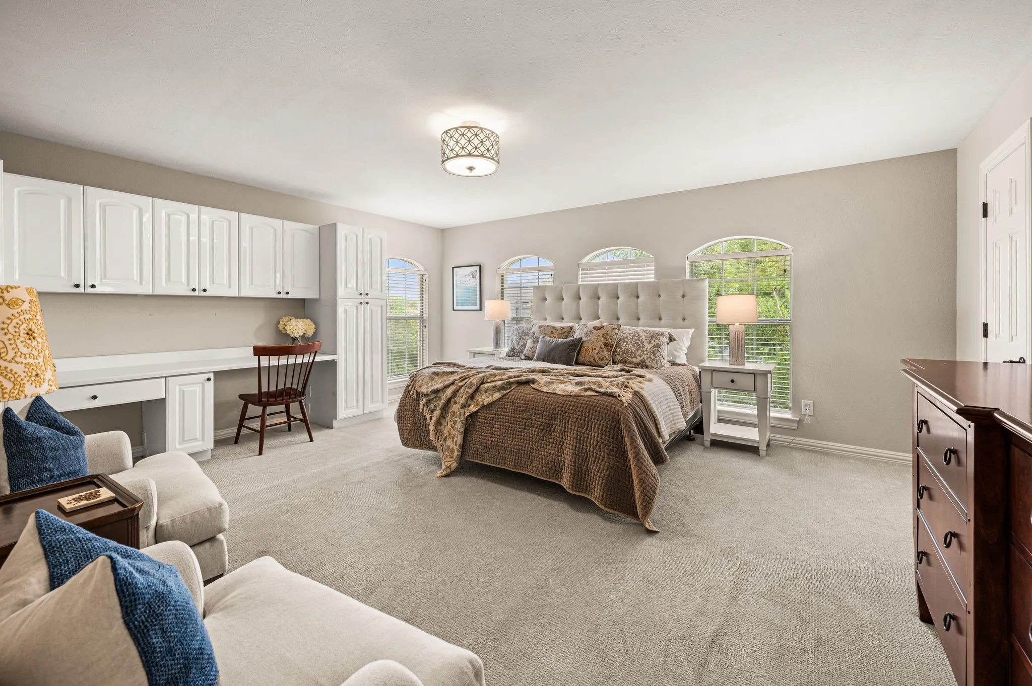 One of the upstairs bedrooms offers generous proportions, built-in workspace and a series of arched windows that bring in views of the surrounding trees.