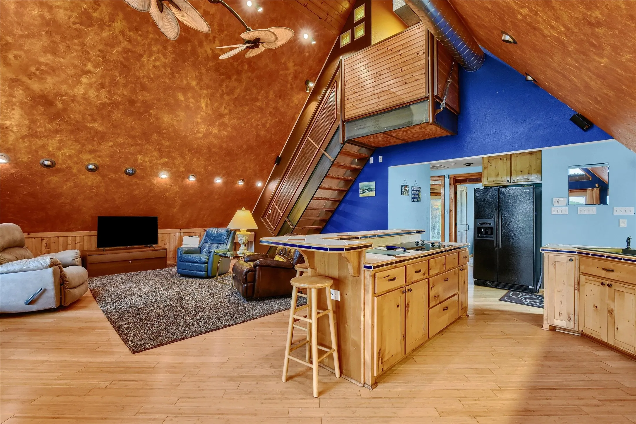 Kitchen featuring high vaulted ceiling, black refrigerator with ice dispenser, a kitchen bar, and light hardwood / wood-style flooring